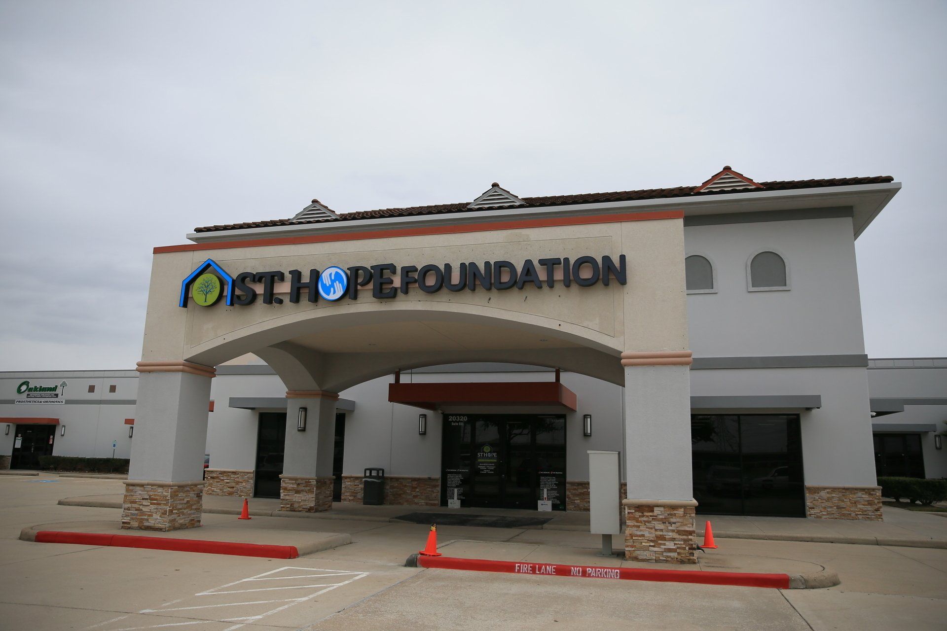 Exterior view of St. Hope Foundation building with a large arched entrance, stone base, and tan and gray exterior walls.