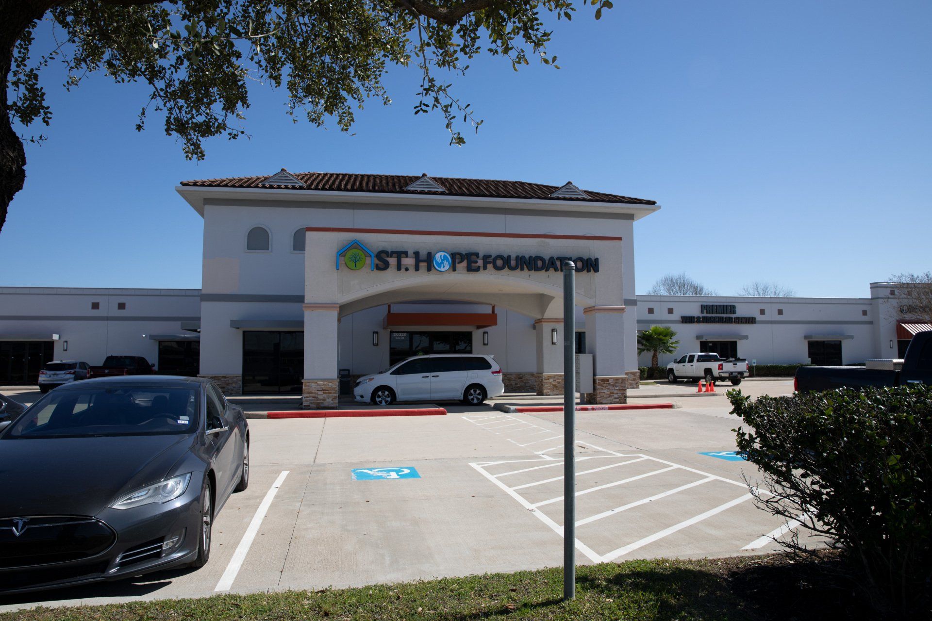 St. Hope Foundation medical clinic building with a parking lot and a parked white van on a sunny day.