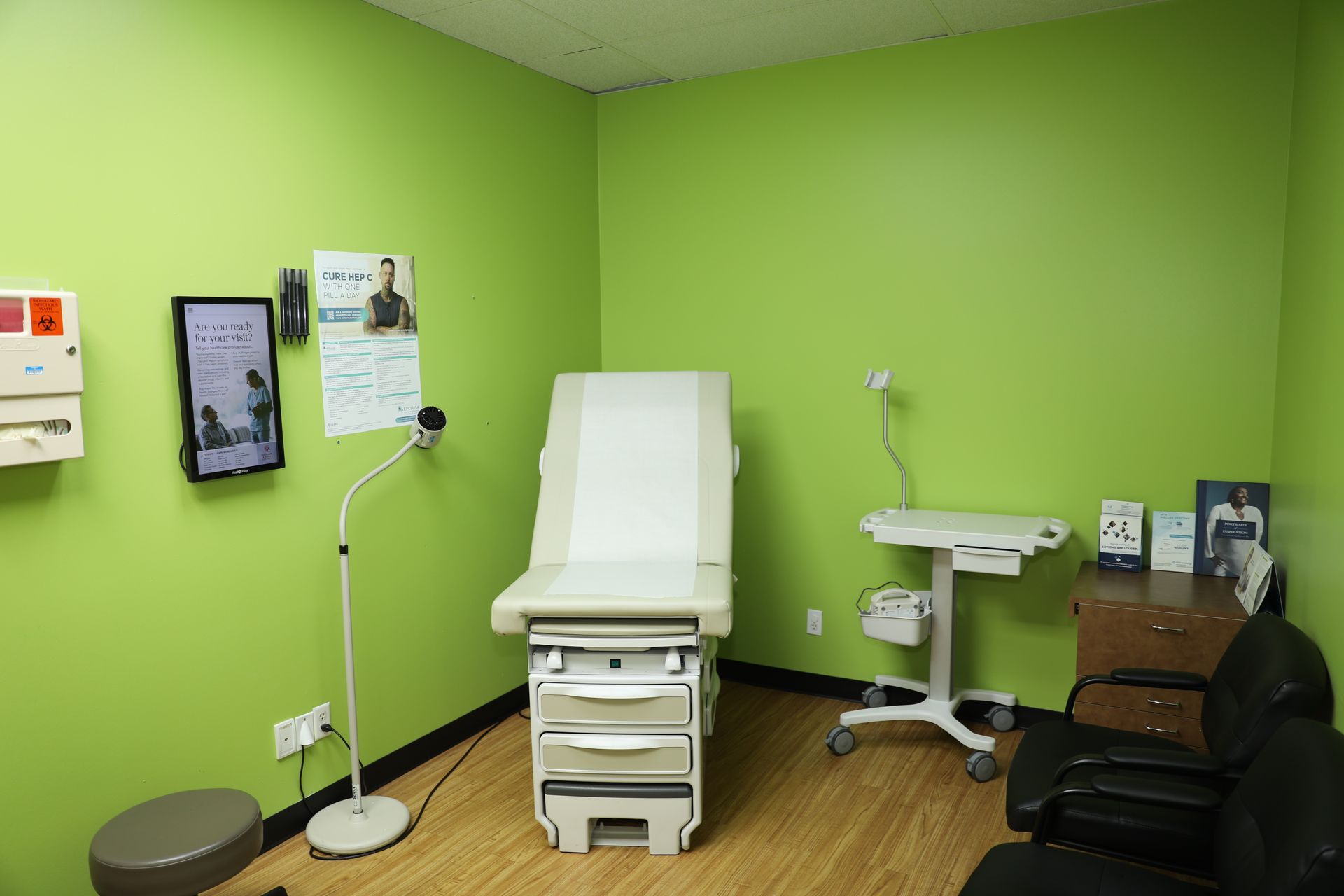 A bright green medical examination room with an exam table, medical equipment, and seating against the wall.