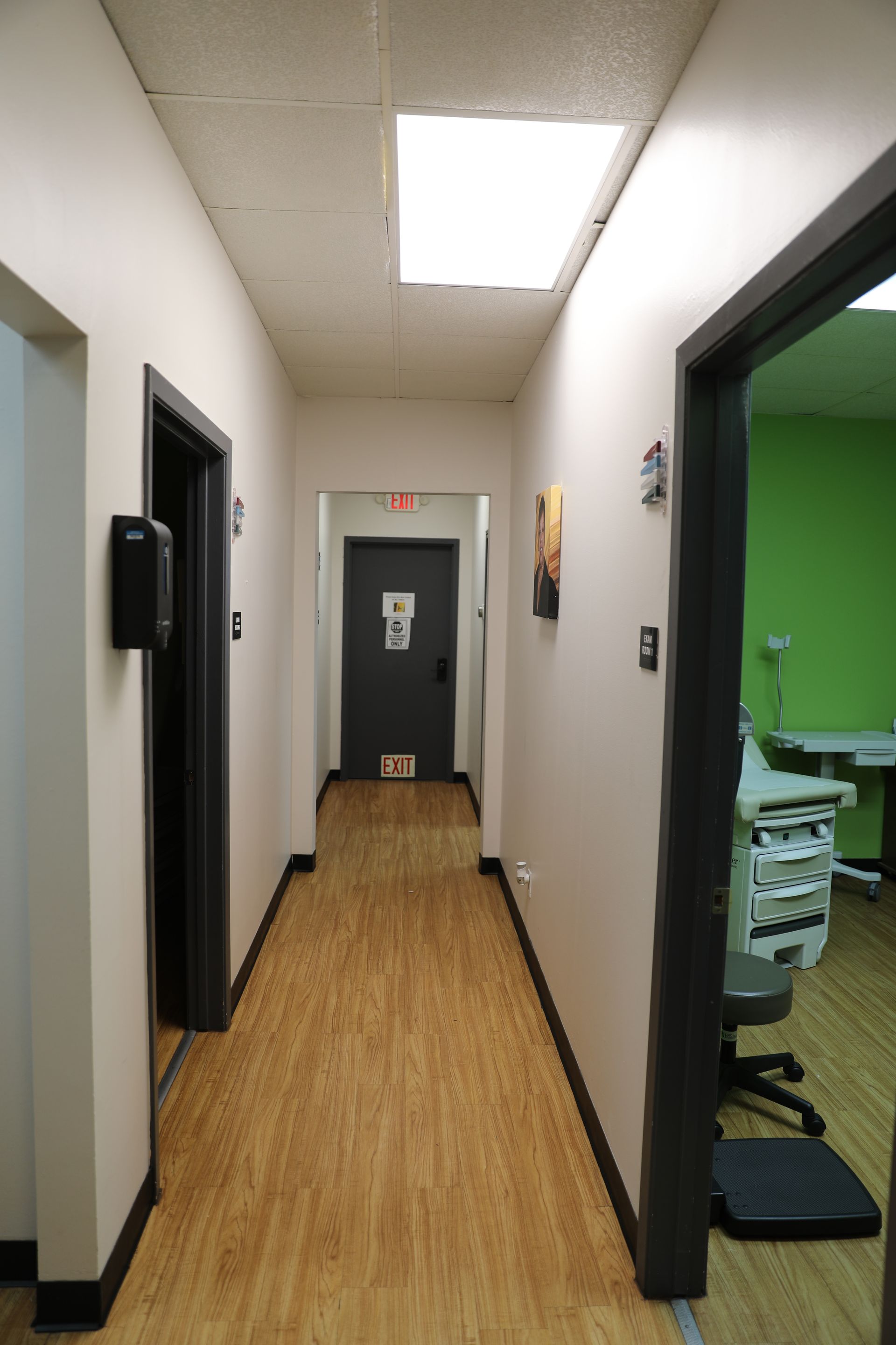 A hallway with light wood flooring, beige walls, and doorways leading to rooms, including one with green walls.