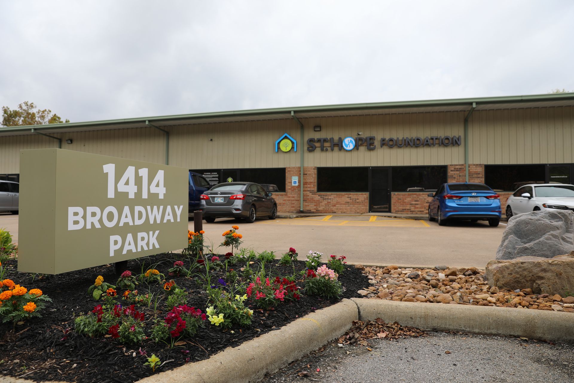 Exterior of the St. Hope Foundation office at 1414 Broadway Park, featuring a tan building with parking and flowers.