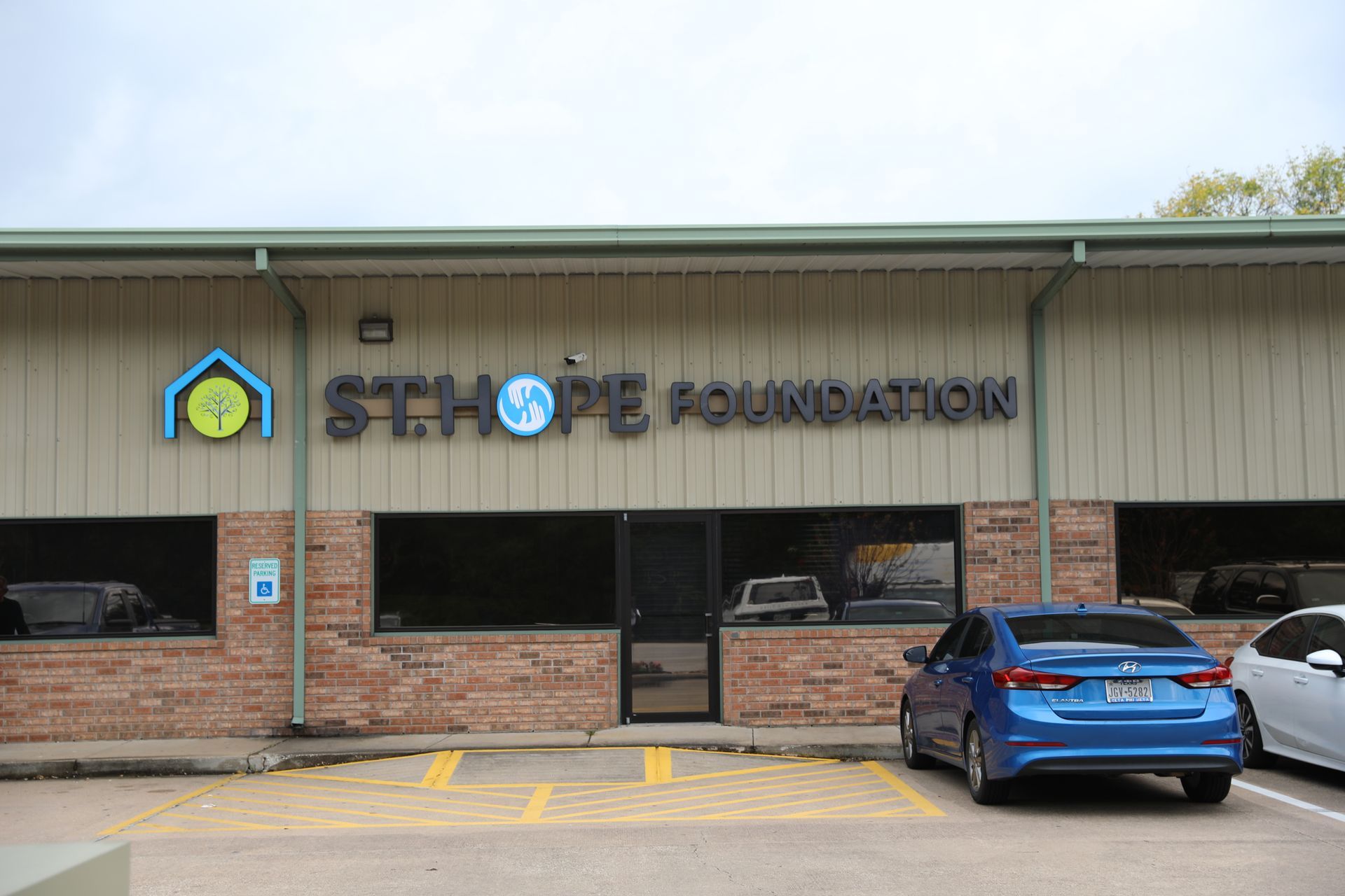 The STHOPE Foundation office building exterior with a blue and white logo, brick accents, and parked cars in the front.