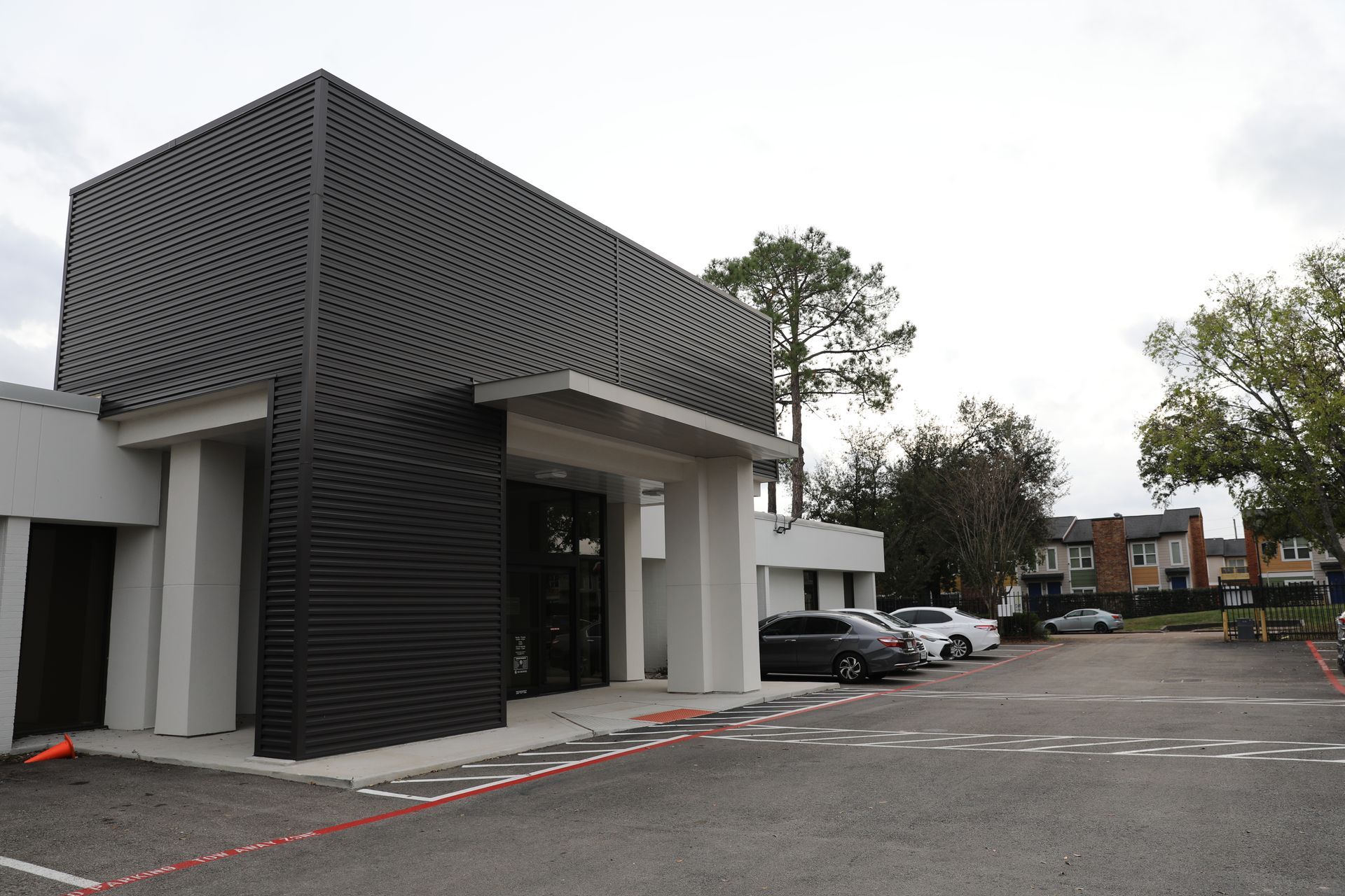 A modern commercial building with a striking black, textured facade and white pillars, set against a parking lot.