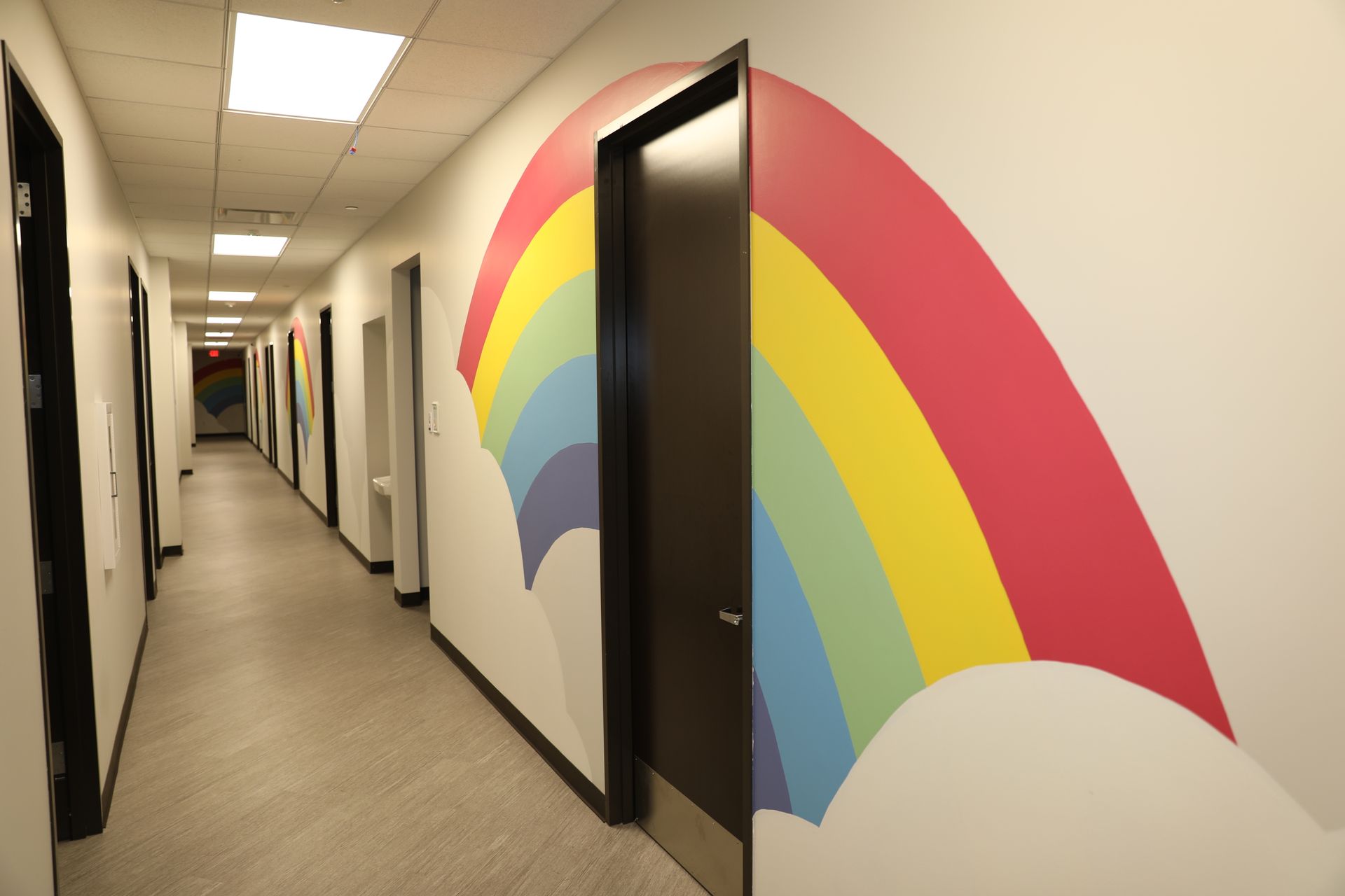 A long hallway with white walls decorated with painted colorful rainbows framing each dark doorway.