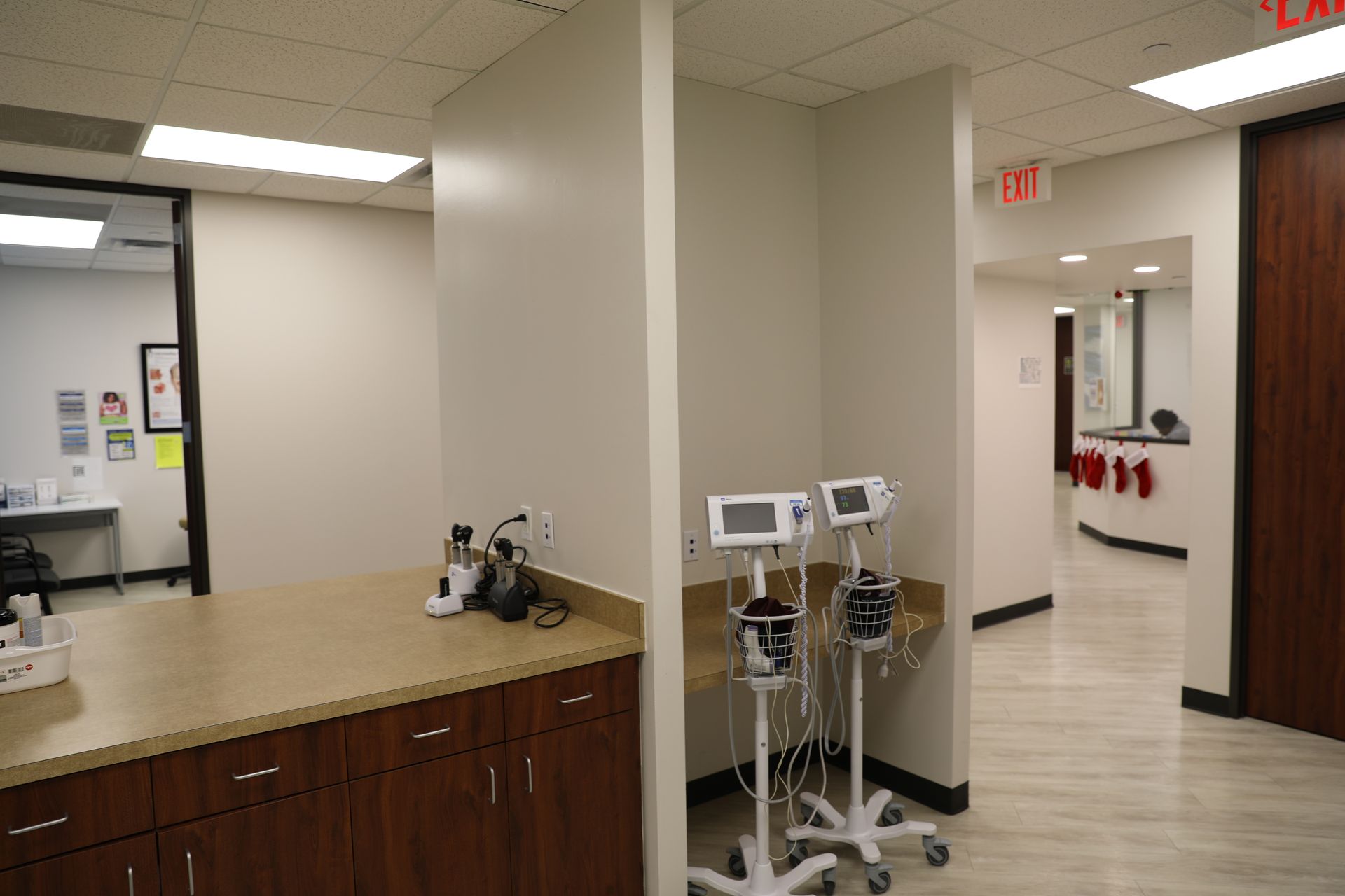 A clinical office hallway with medical equipment, a wooden cabinet, and a view into a reception area.