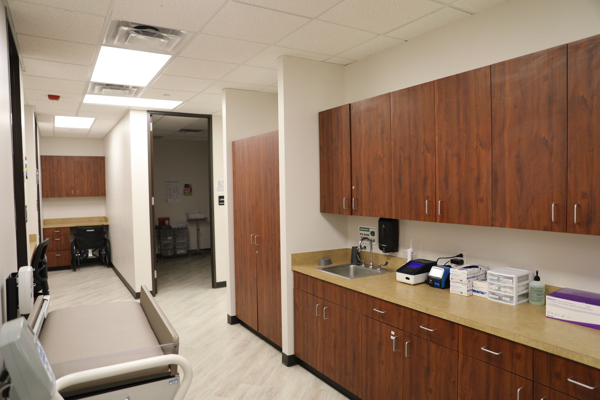 An examination room featuring wooden cabinetry, a sink, a medical exam table, and an open doorway to a hallway.