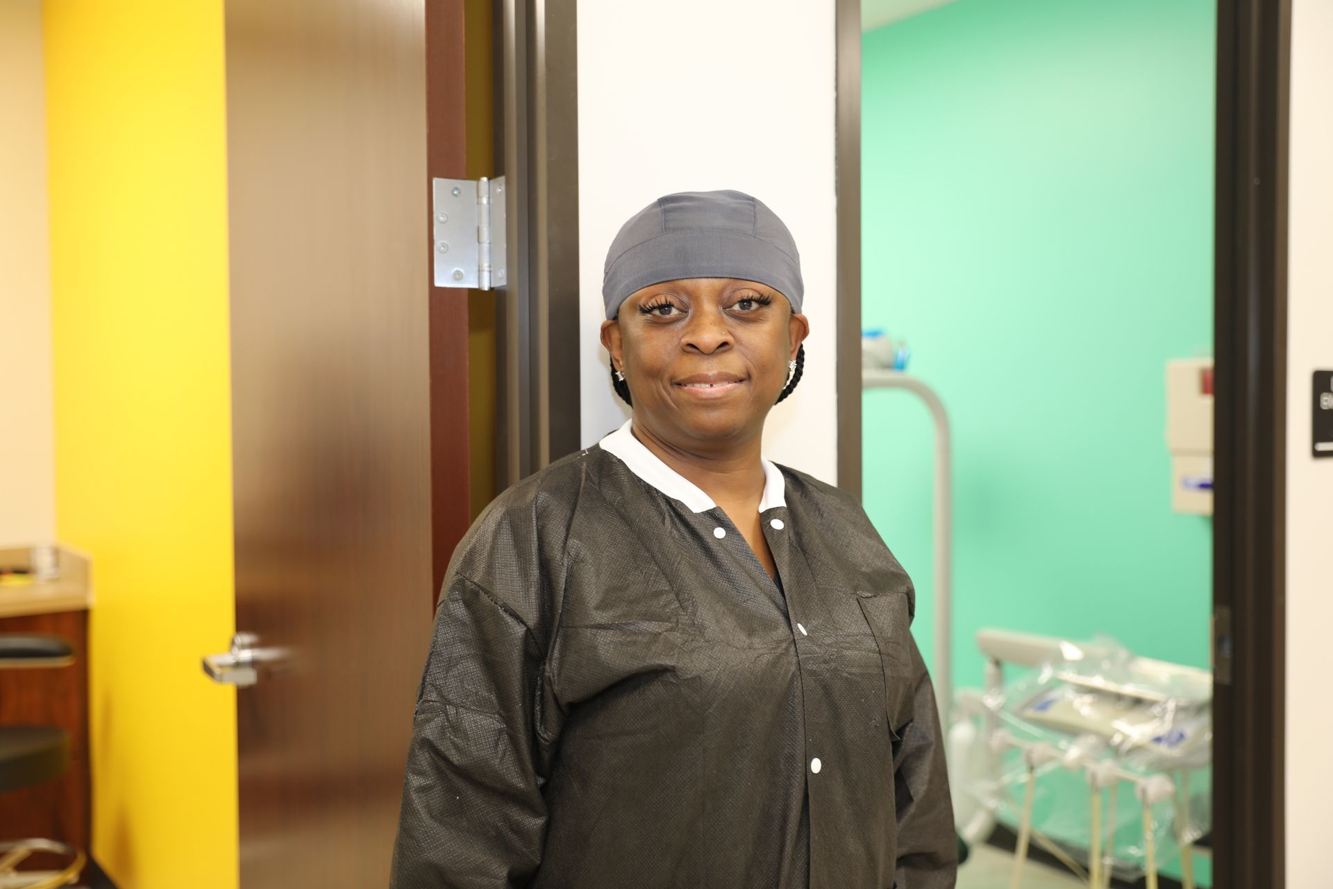 A person wearing a grey cap and black medical scrub top stands in a doorway between a yellow room and a mint green room.