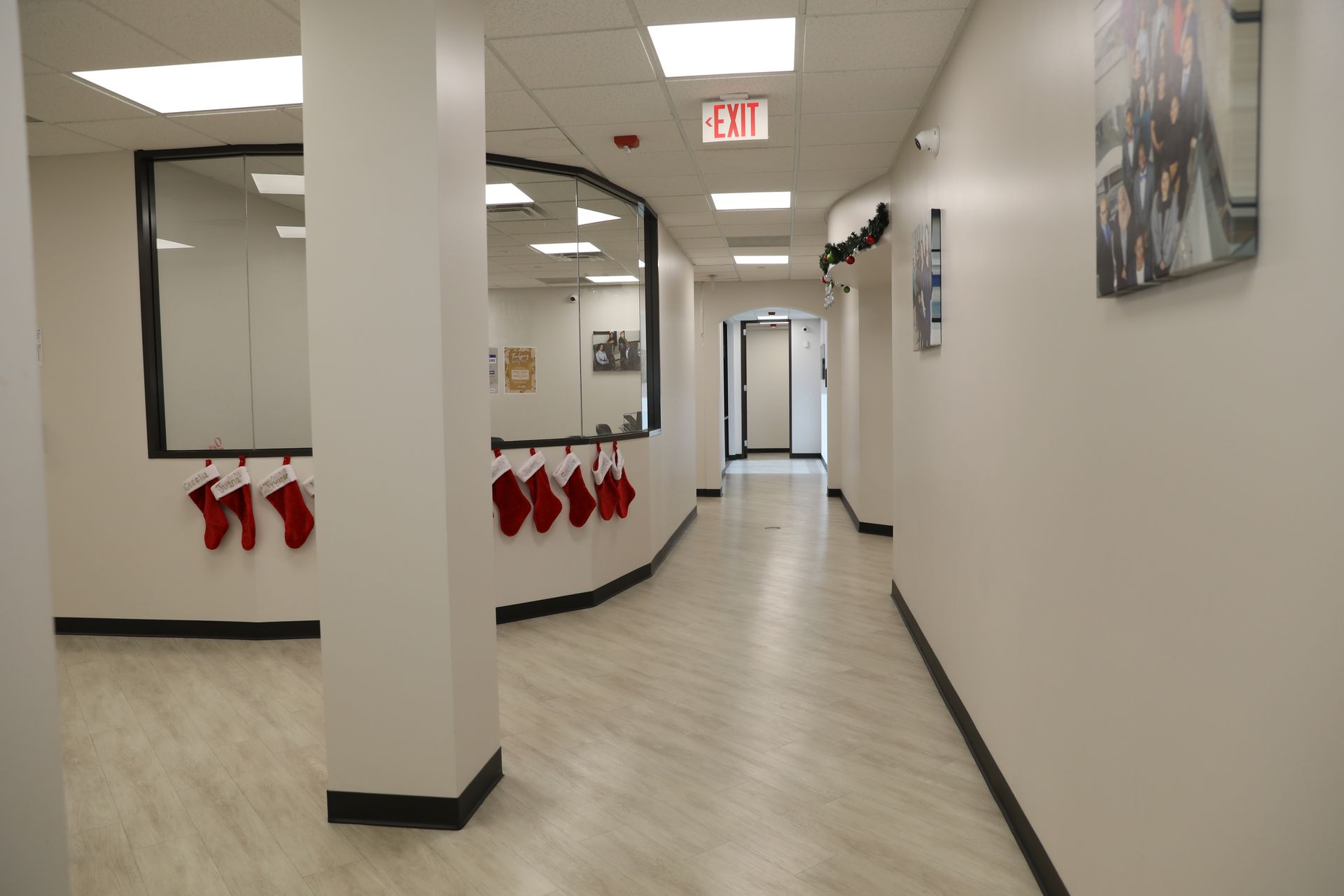 A bright, modern hallway with wood-look floors, a large interior window, and red Christmas stockings hanging on a railing.