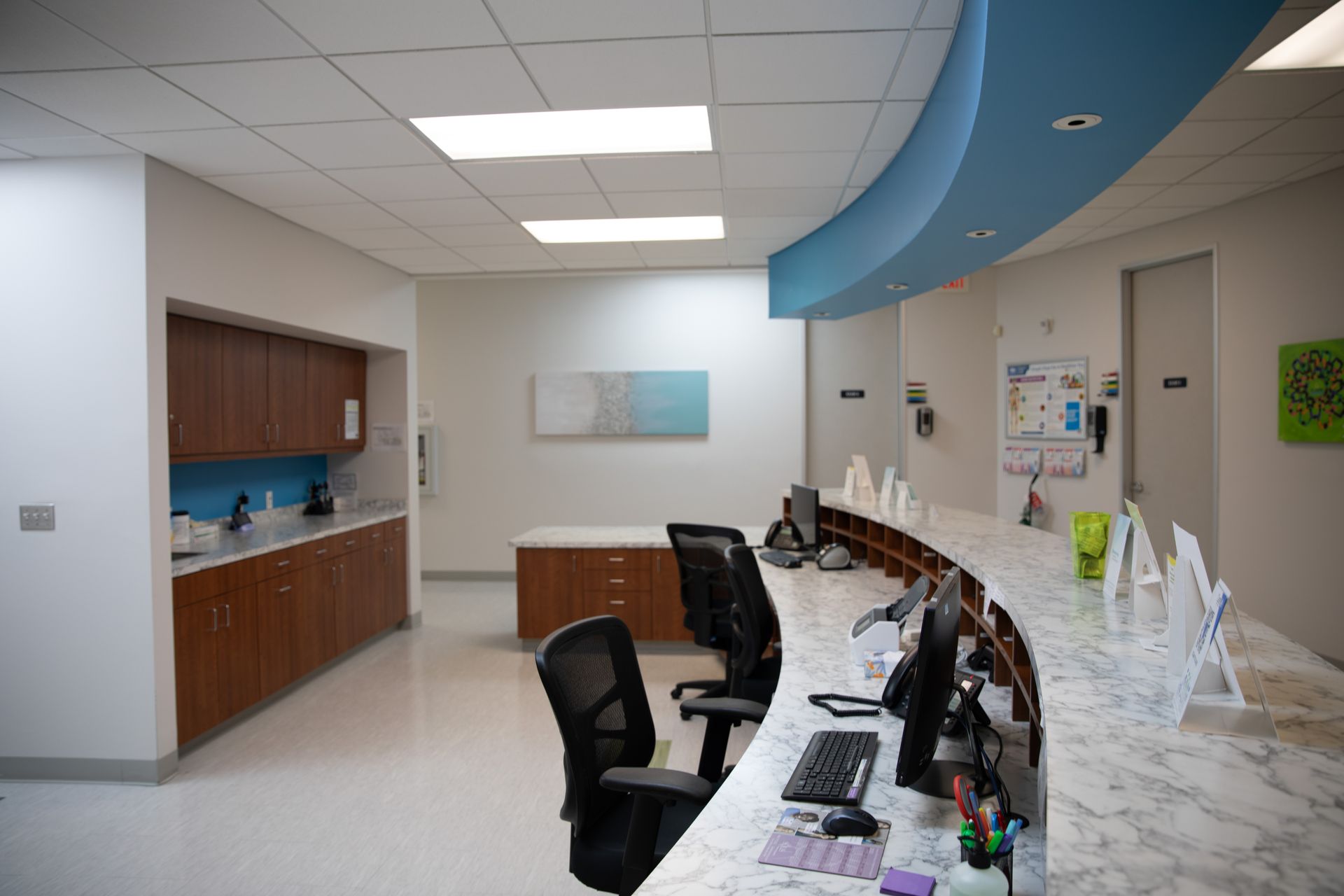 A bright reception desk with chairs, marble-patterned countertops, and wooden cabinetry in a clinical office setting.