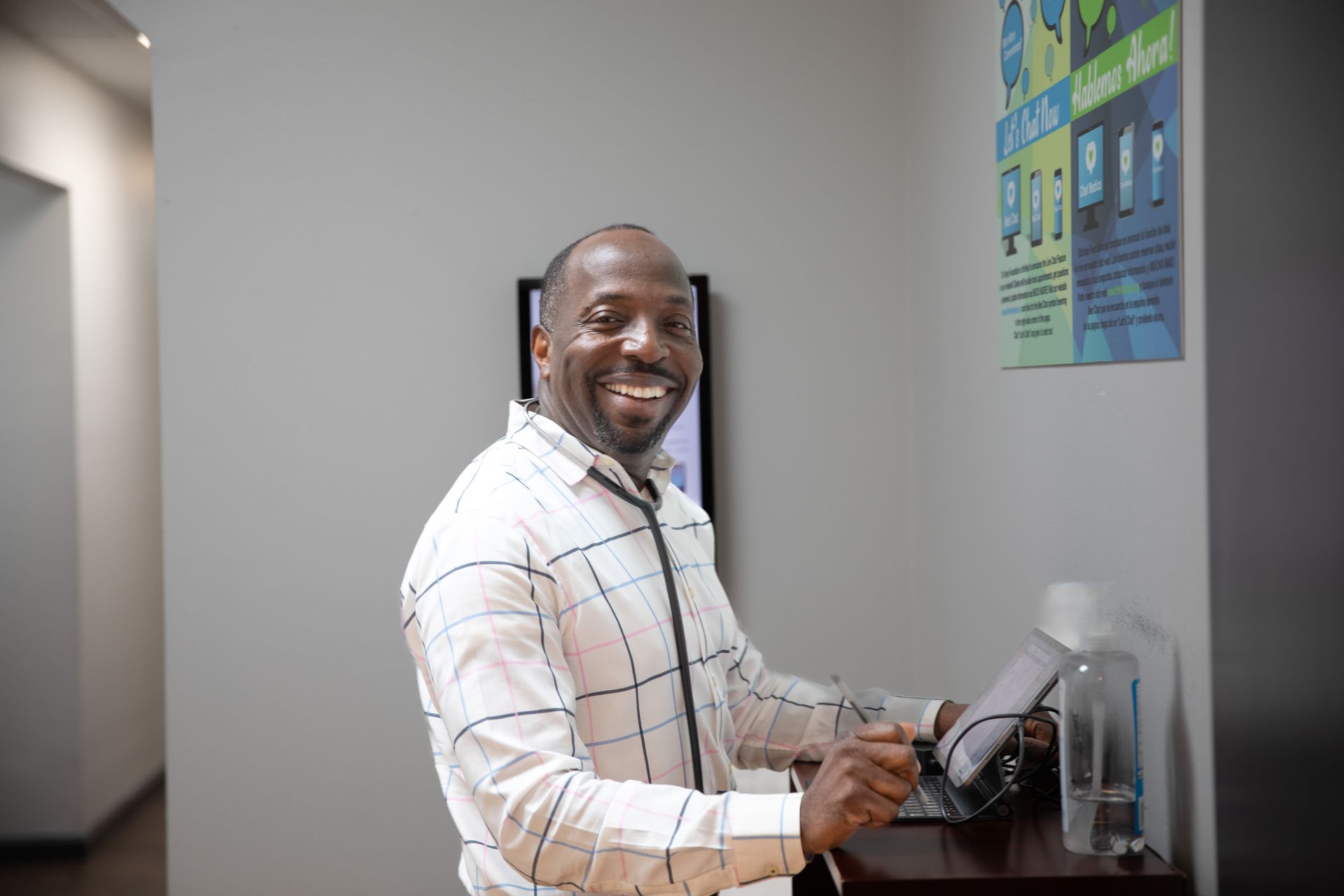 A professional in a white patterned shirt and stethoscope smiling while reviewing digital records in an office.