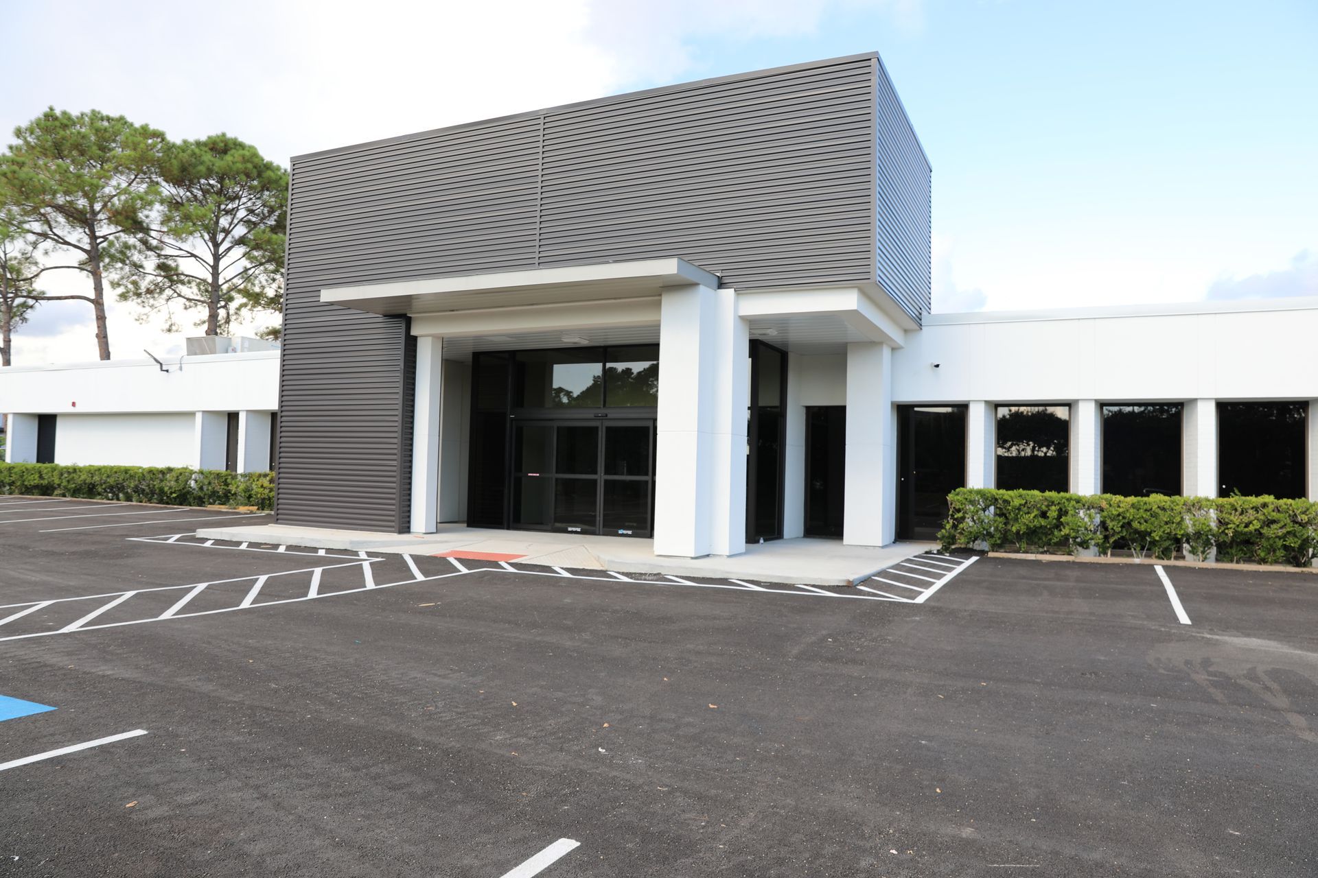 Modern one-story commercial building exterior with a textured, wavy dark gray entrance and white concrete walls.