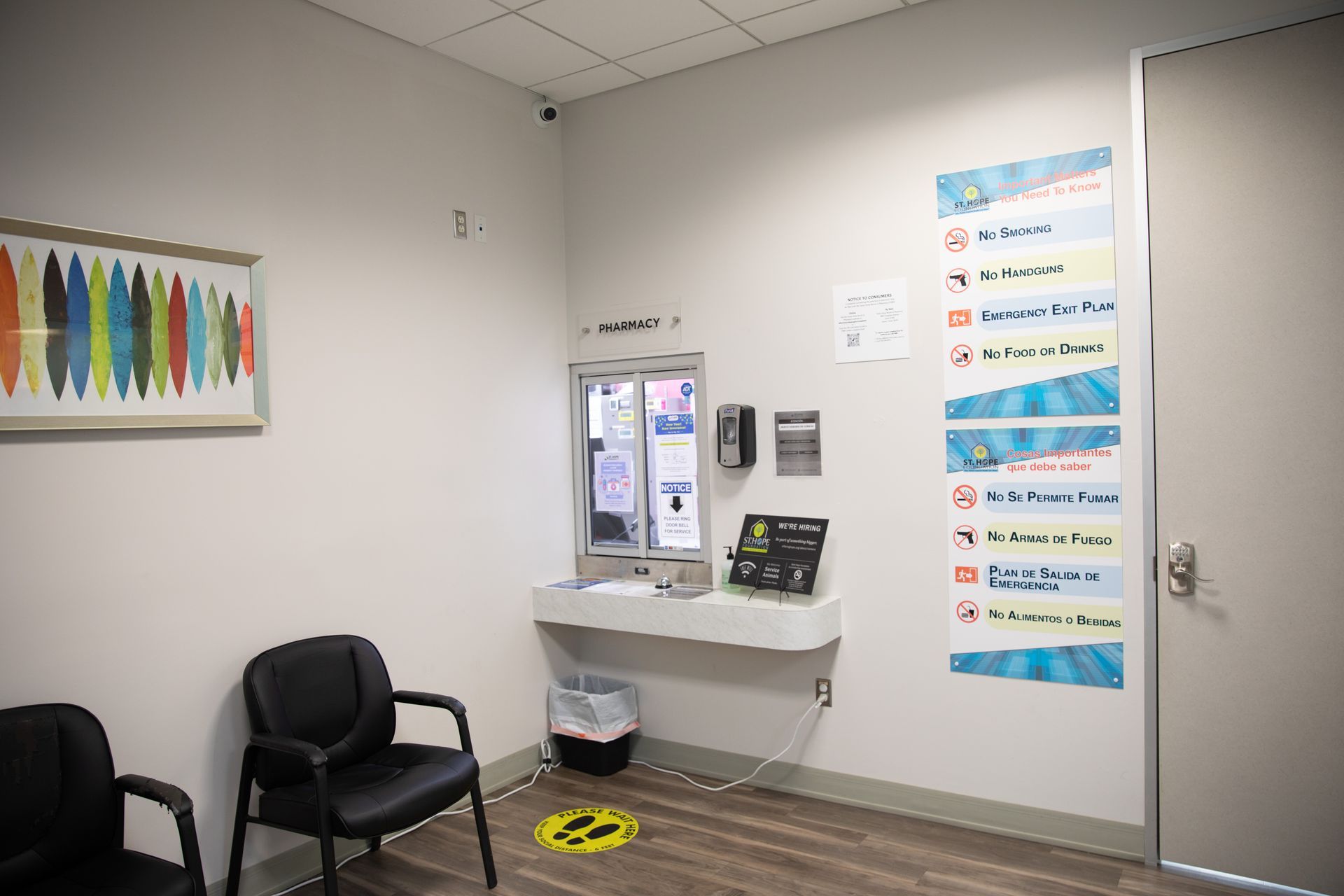 A waiting area with two chairs, a reception window, a trash can, and a vertical sign detailing office policies.