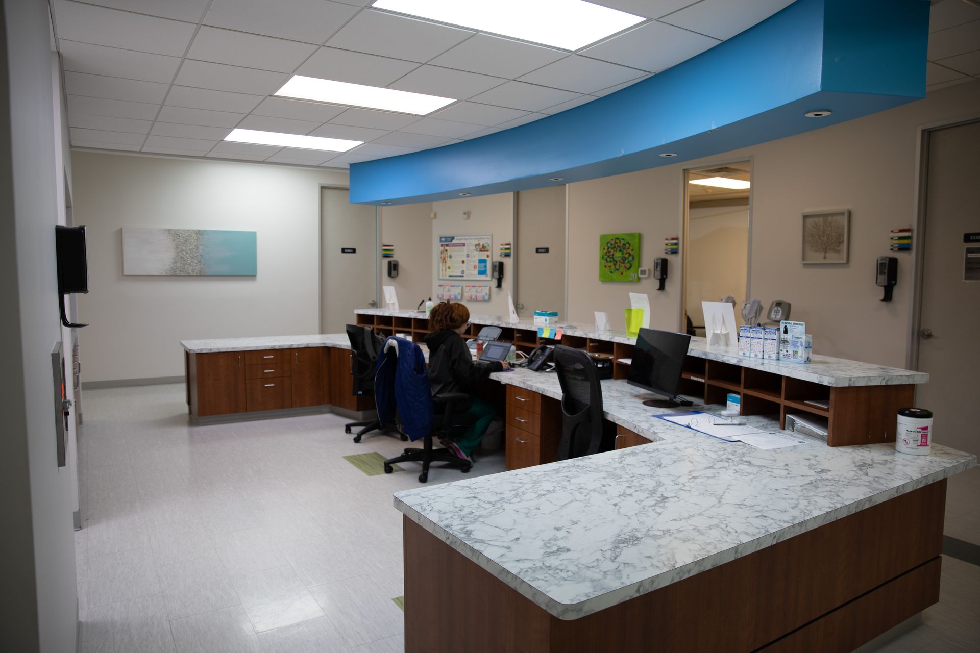 A bright, modern medical reception desk with wood cabinets, stone countertops, and a staff member working at a computer.