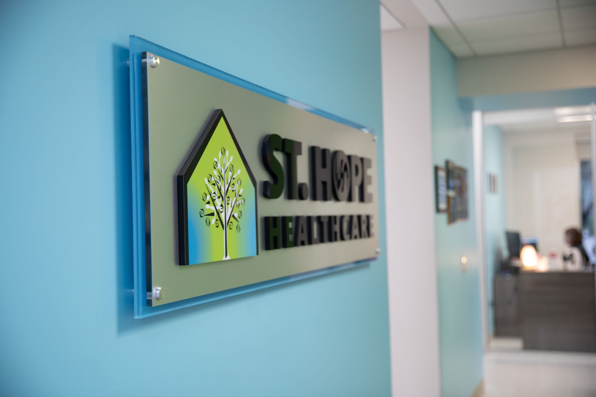 A St. Hope Healthcare sign with a tree logo on a blue wall, with a reception desk visible in the background.