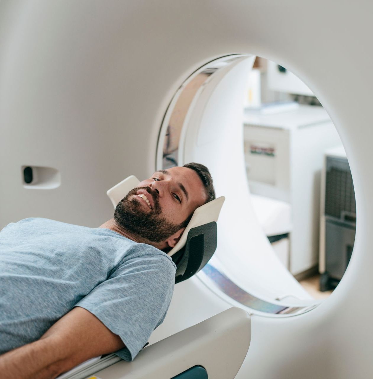 A smiling person lying in a medical imaging scanner for a CT or MRI scan.