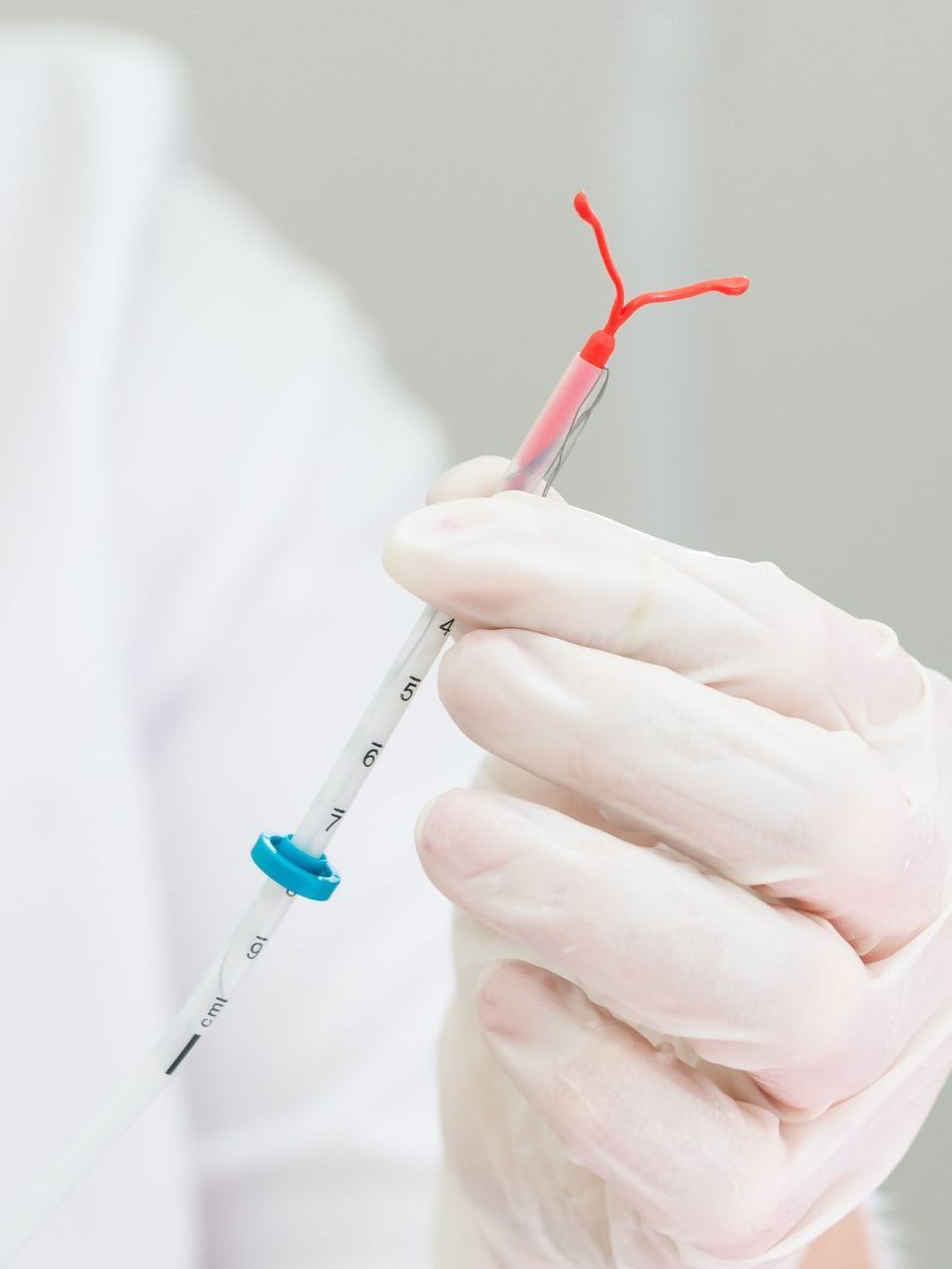 A gloved hand holds an intrauterine device (IUD) inside its applicator tube.