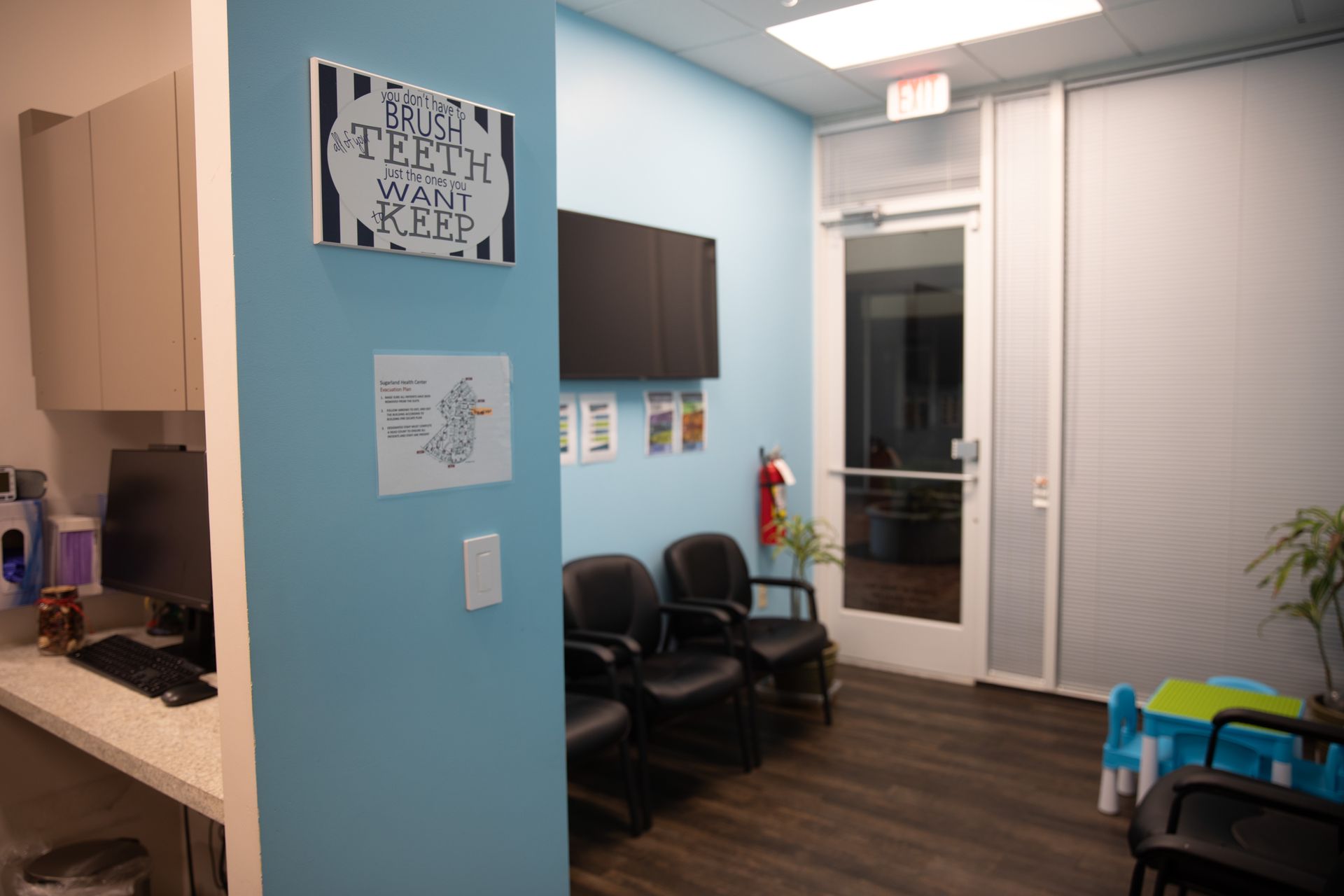 A waiting room with blue walls, black chairs, a sign about brushing teeth, a glass door, and a small play table.