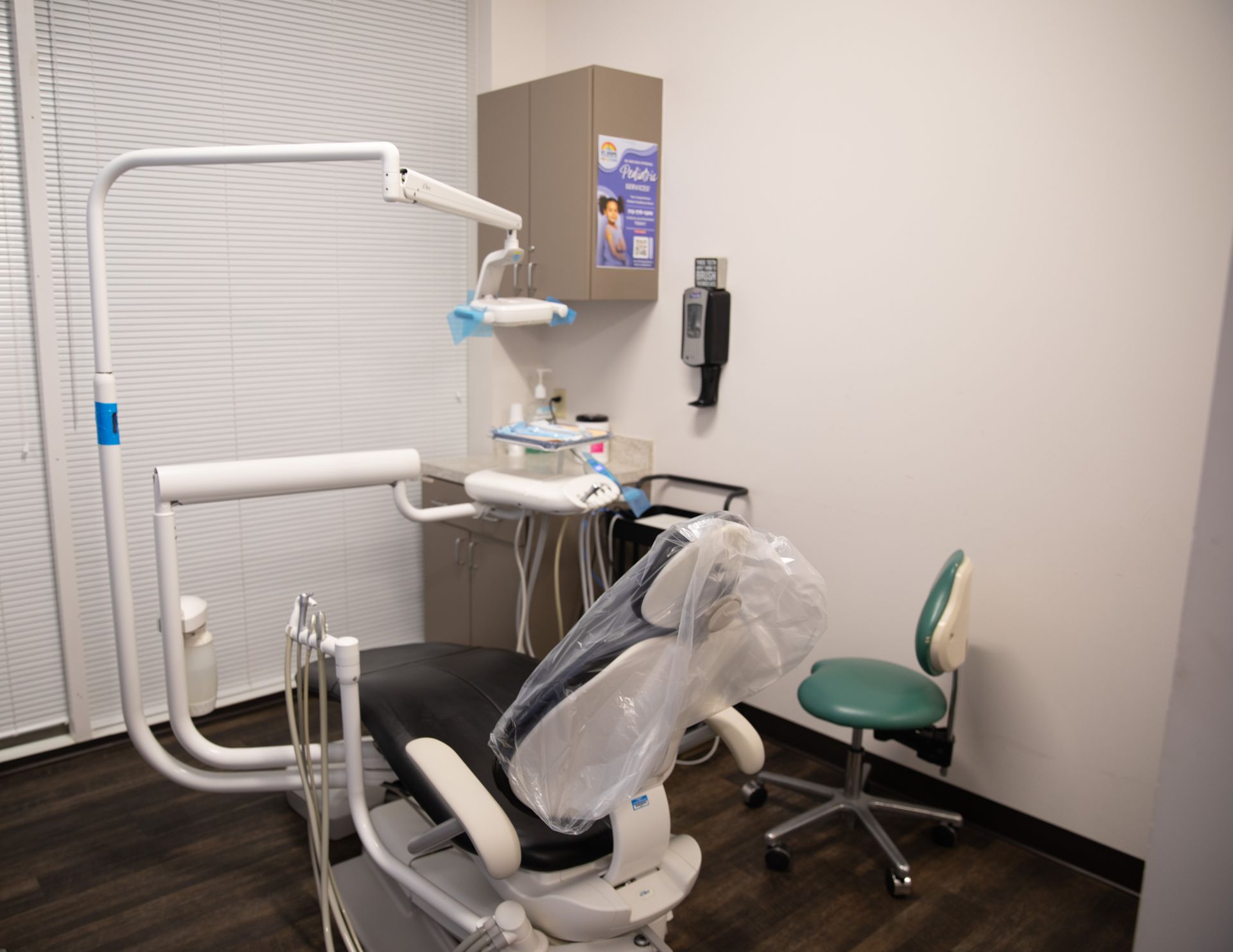 A dental examination room with a patient chair, dental equipment, and a green stool on a dark wood floor.