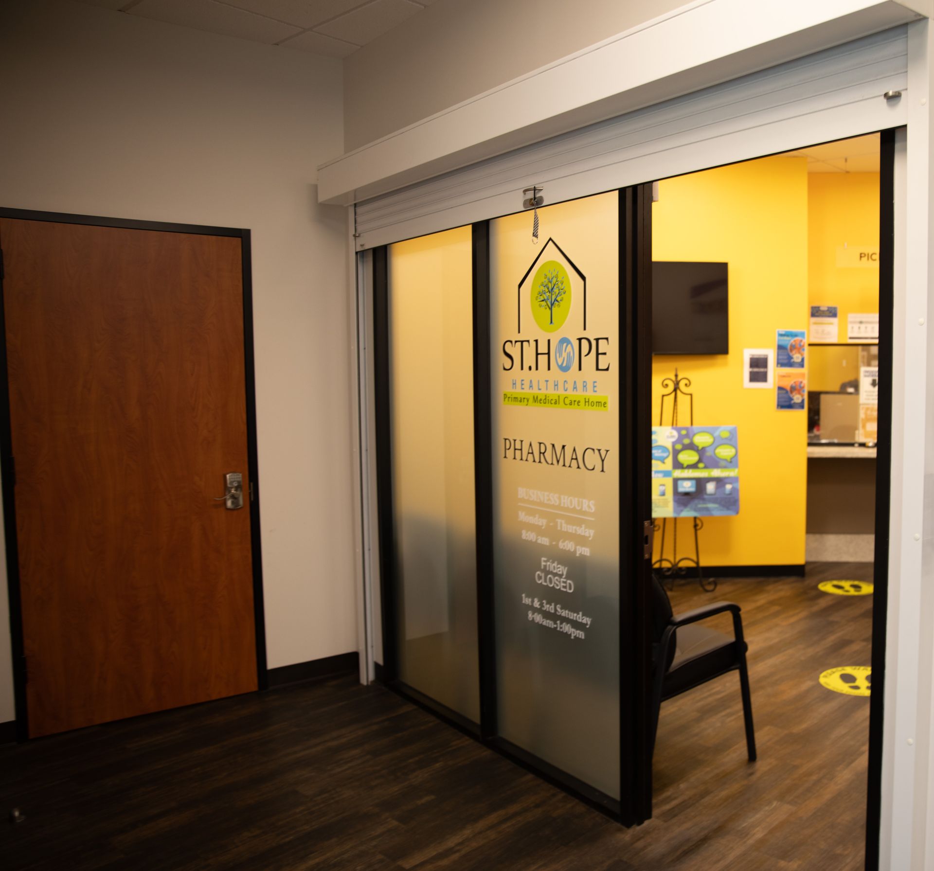 An entrance to a St. Hope Pharmacy with a glass door, yellow walls, and a waiting area inside.