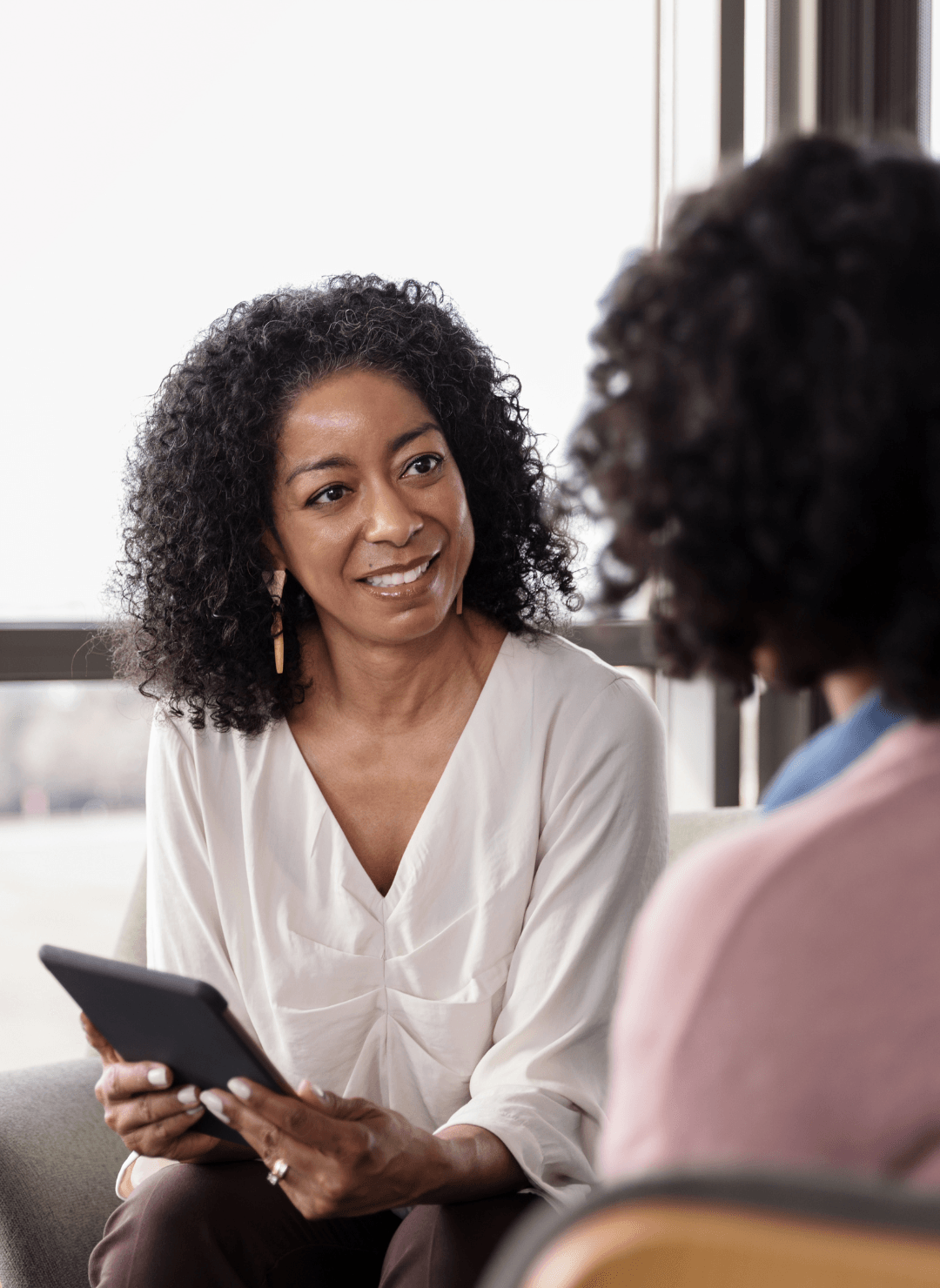 A professional holding a tablet smiles while engaged in conversation with someone sitting across from them.