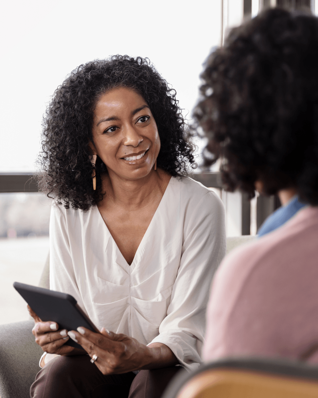 Two people sit facing each other, one holding a tablet and smiling during a professional consultation.
