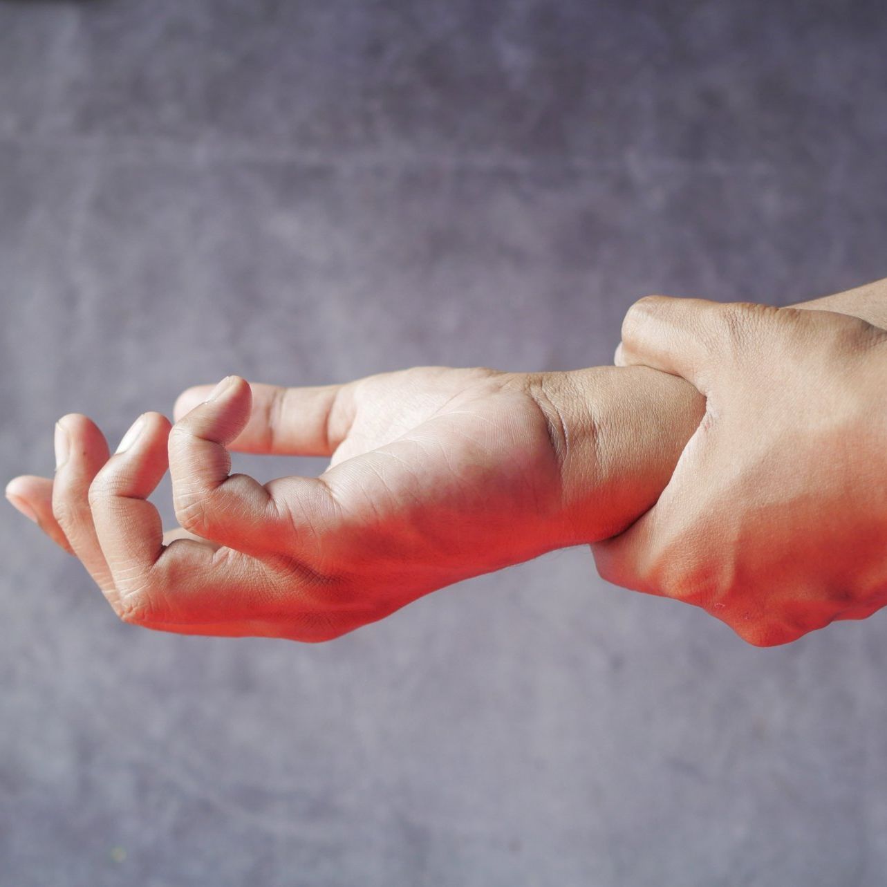 A person's right hand grasps their left wrist against a textured grey background.