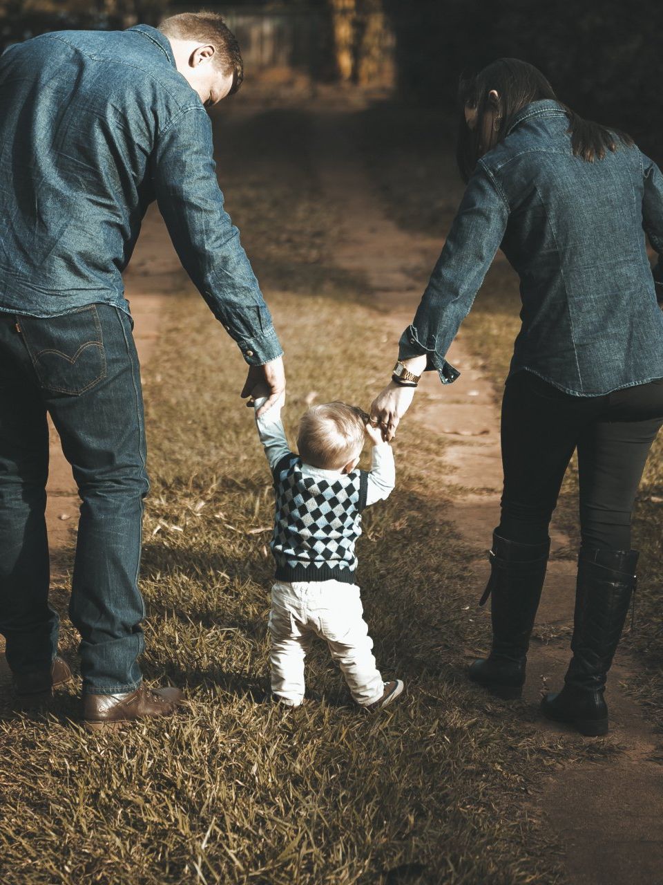 A couple holding hands with a toddler walking between them on a dirt path.