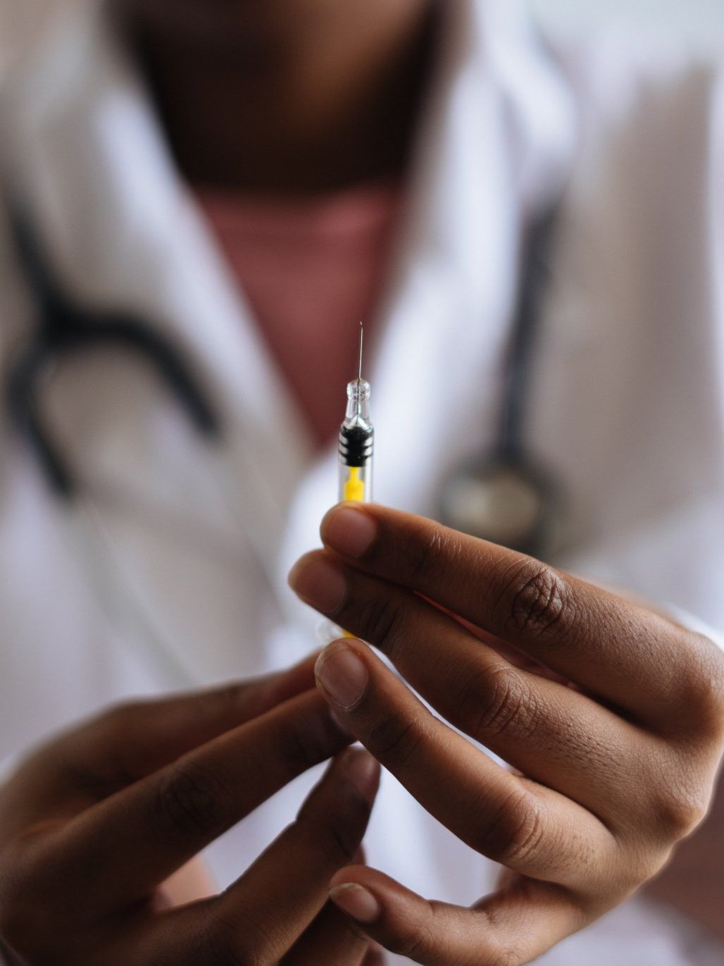 A person in a white lab coat holds a syringe with yellow liquid, preparing for an injection.