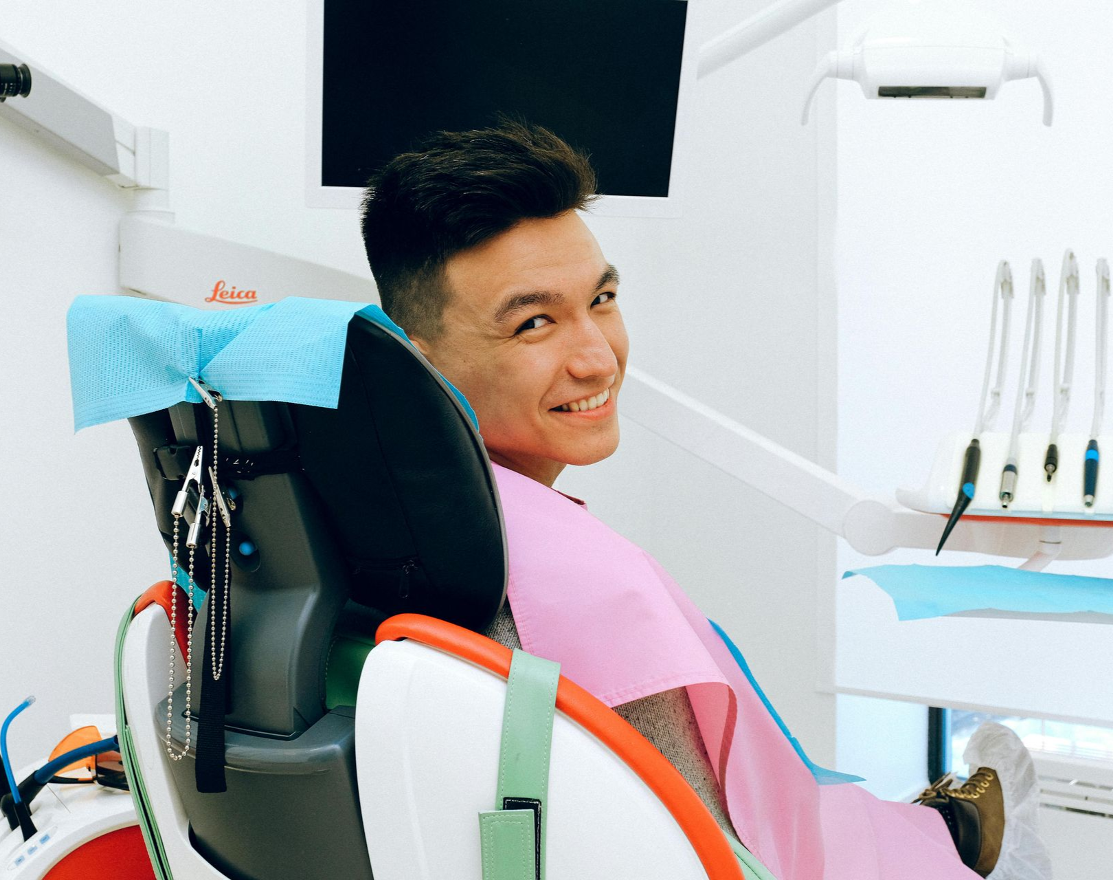 A person wearing a pink bib smiles while sitting in a dentist's chair in a clinic.