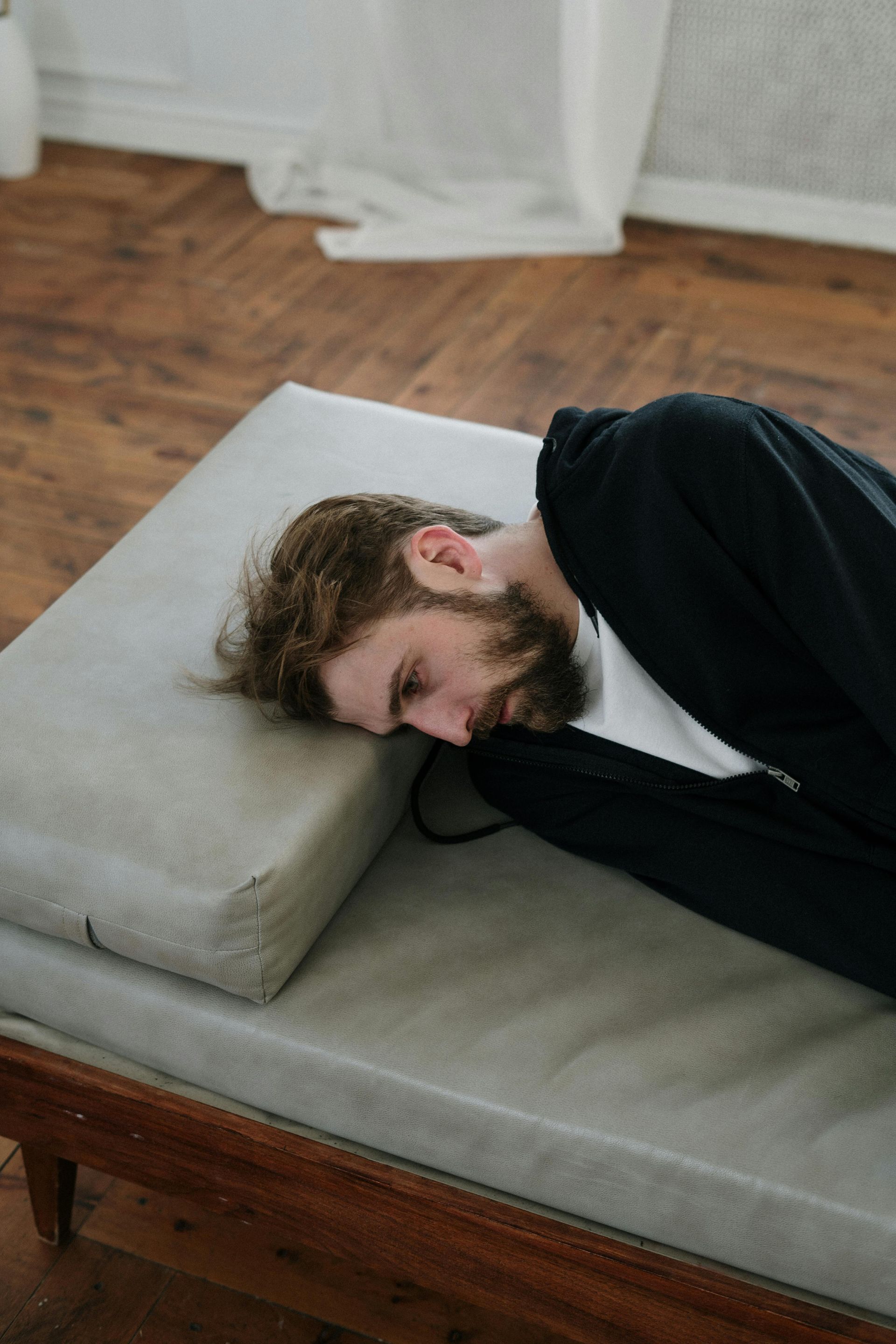 A person with a beard resting their head on a light gray pillow on a wooden daybed.