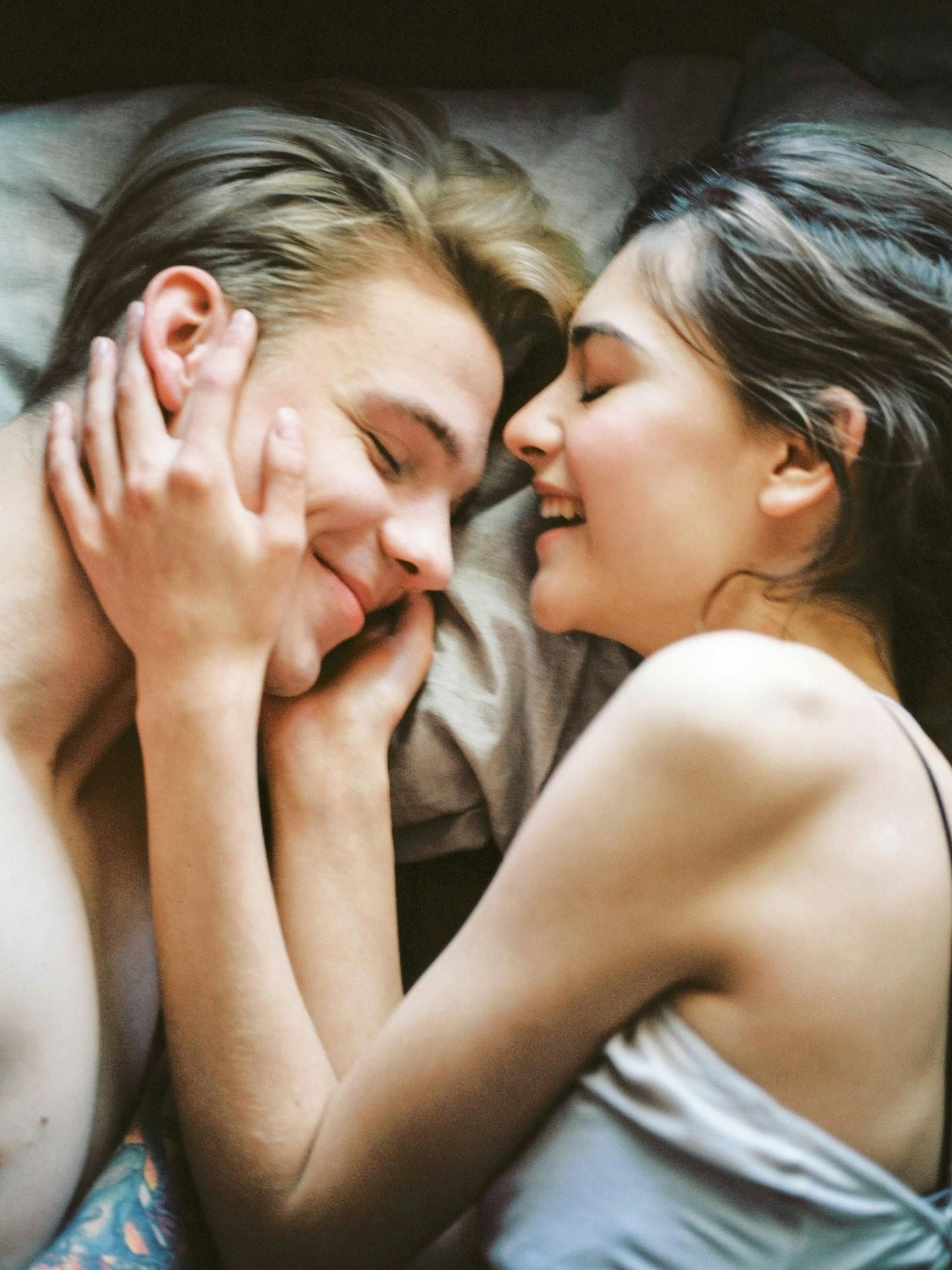 Two people lie together, smiling warmly as one gently holds the other's face.