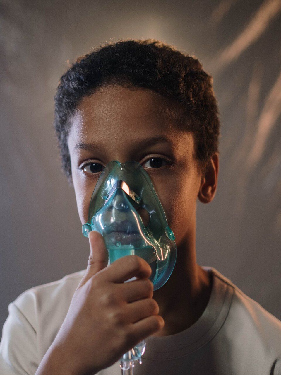 A person holds a green plastic oxygen mask over their face, looking directly at the camera against a neutral background.