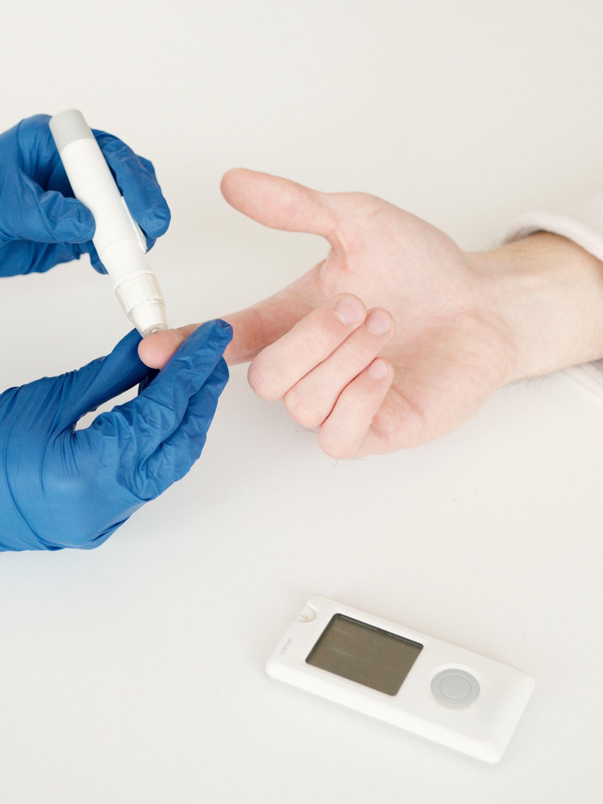A person wearing blue medical gloves uses a lancing device on a finger to prepare for a blood glucose test.