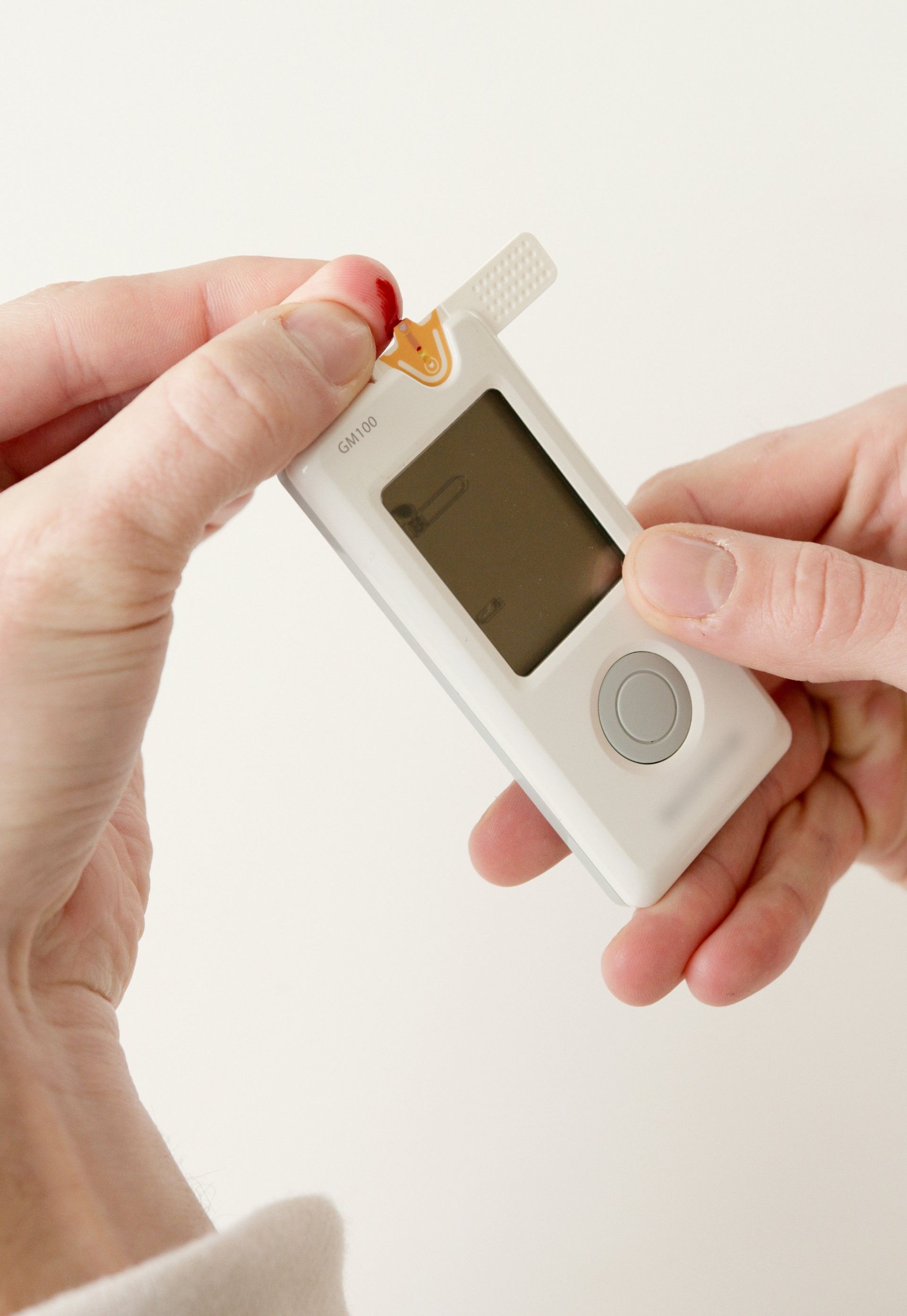 A person uses a white digital blood glucose meter to test a drop of blood on their fingertip.