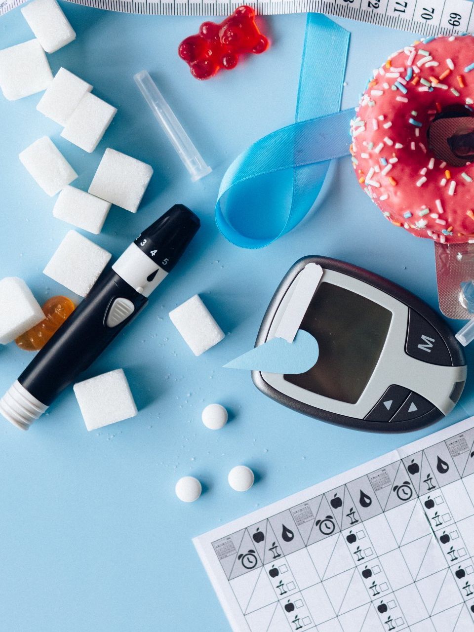 Diabetes management supplies, including a glucometer, lancet, pills, and sugar cubes, arranged on a light blue background.