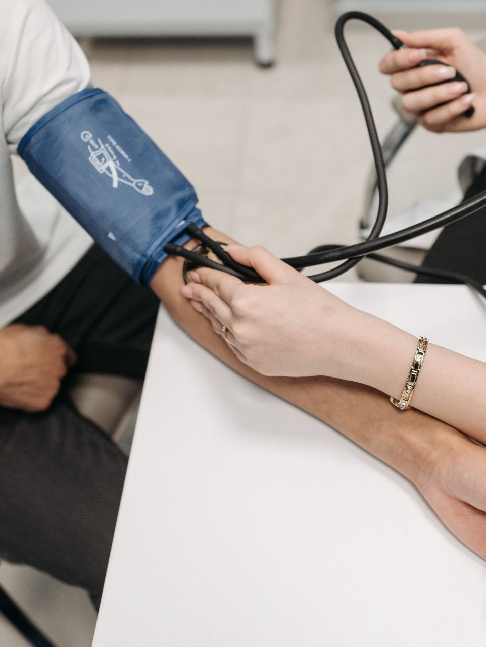 A person’s blood pressure is measured with a blue manual cuff on their upper arm in a clinical setting.