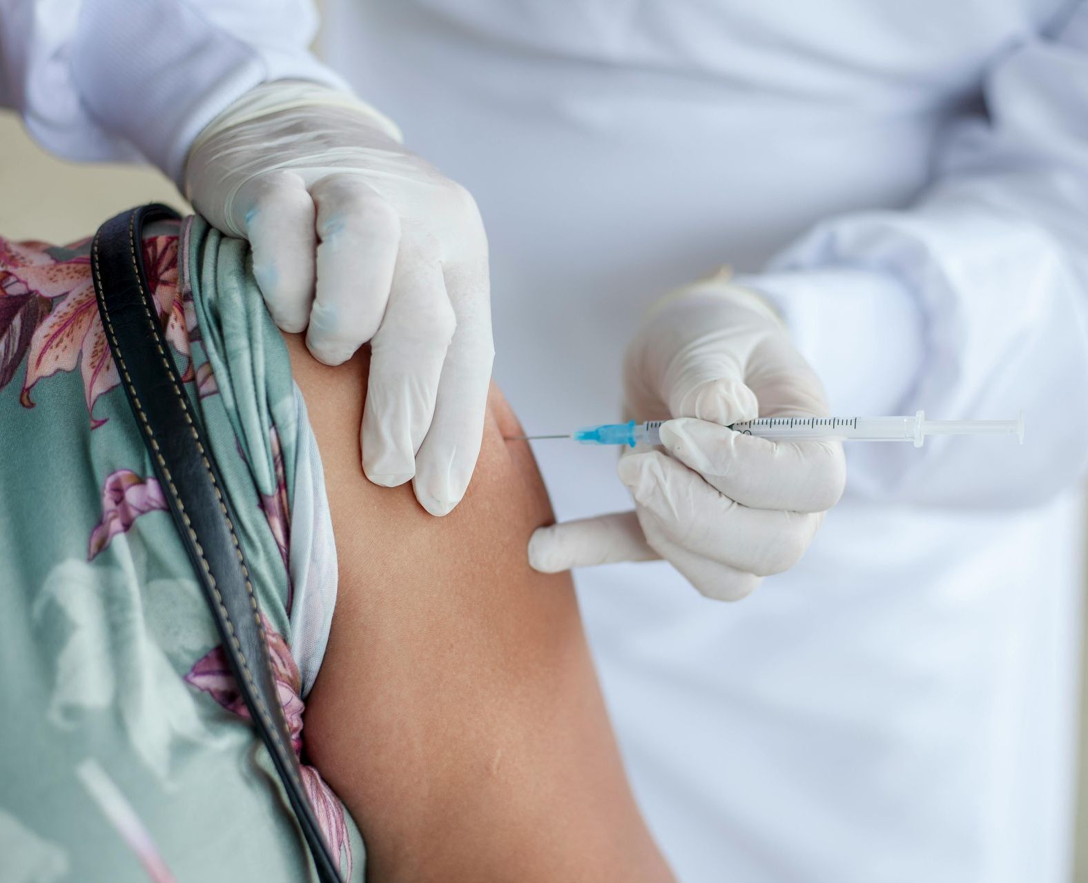 A medical professional in a white coat and gloves administering a vaccine into a patient’s upper arm.