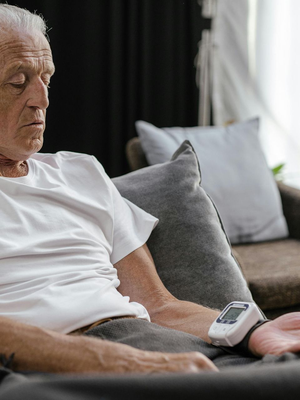 A person sitting in a living room while using a digital wrist blood pressure monitor.
