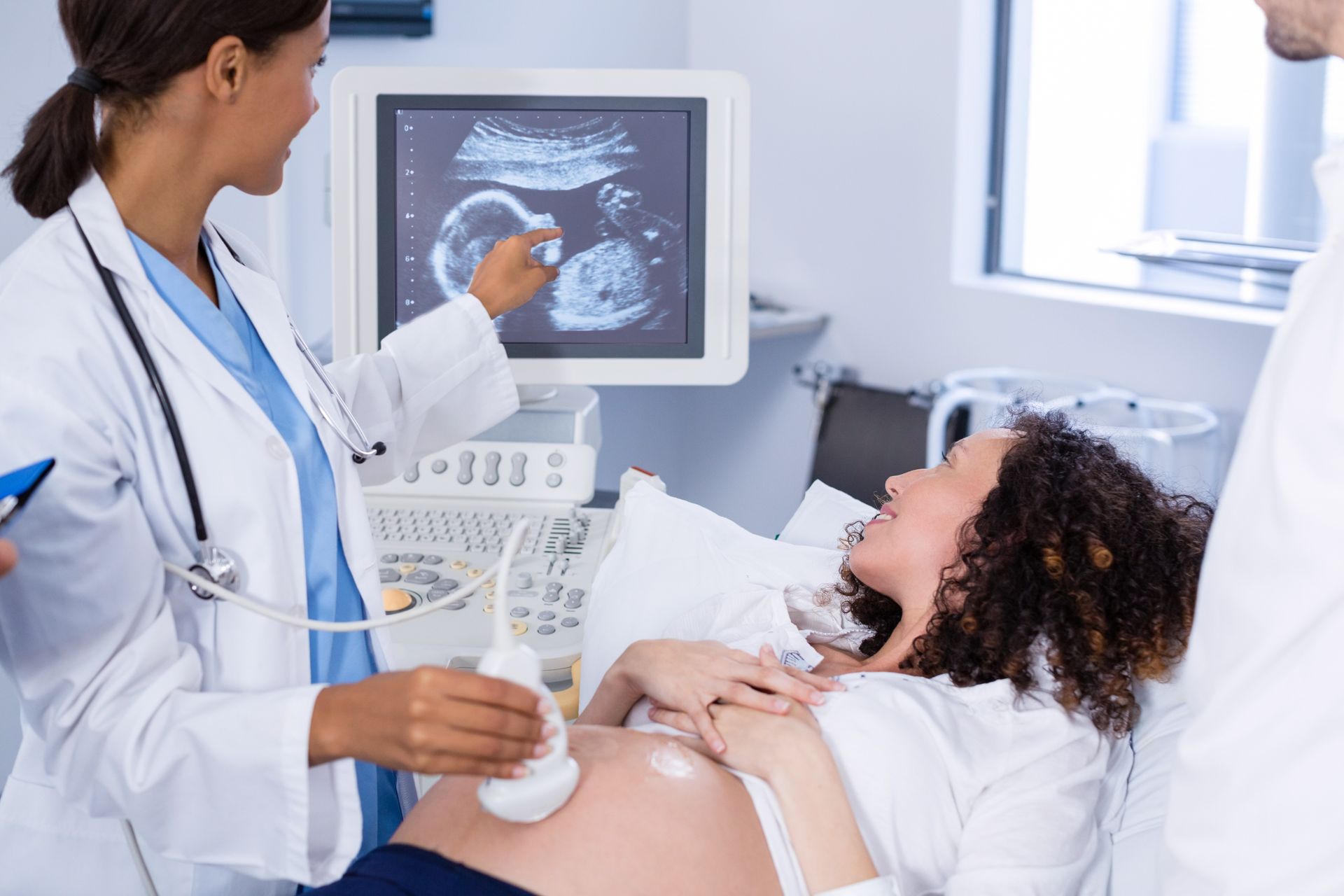A medical professional performs an ultrasound on a pregnant patient, pointing to the monitor showing a developing fetus.