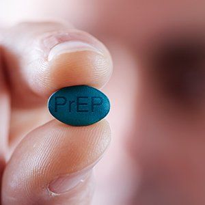 A person holds a small, oval-shaped blue pill with the letters 