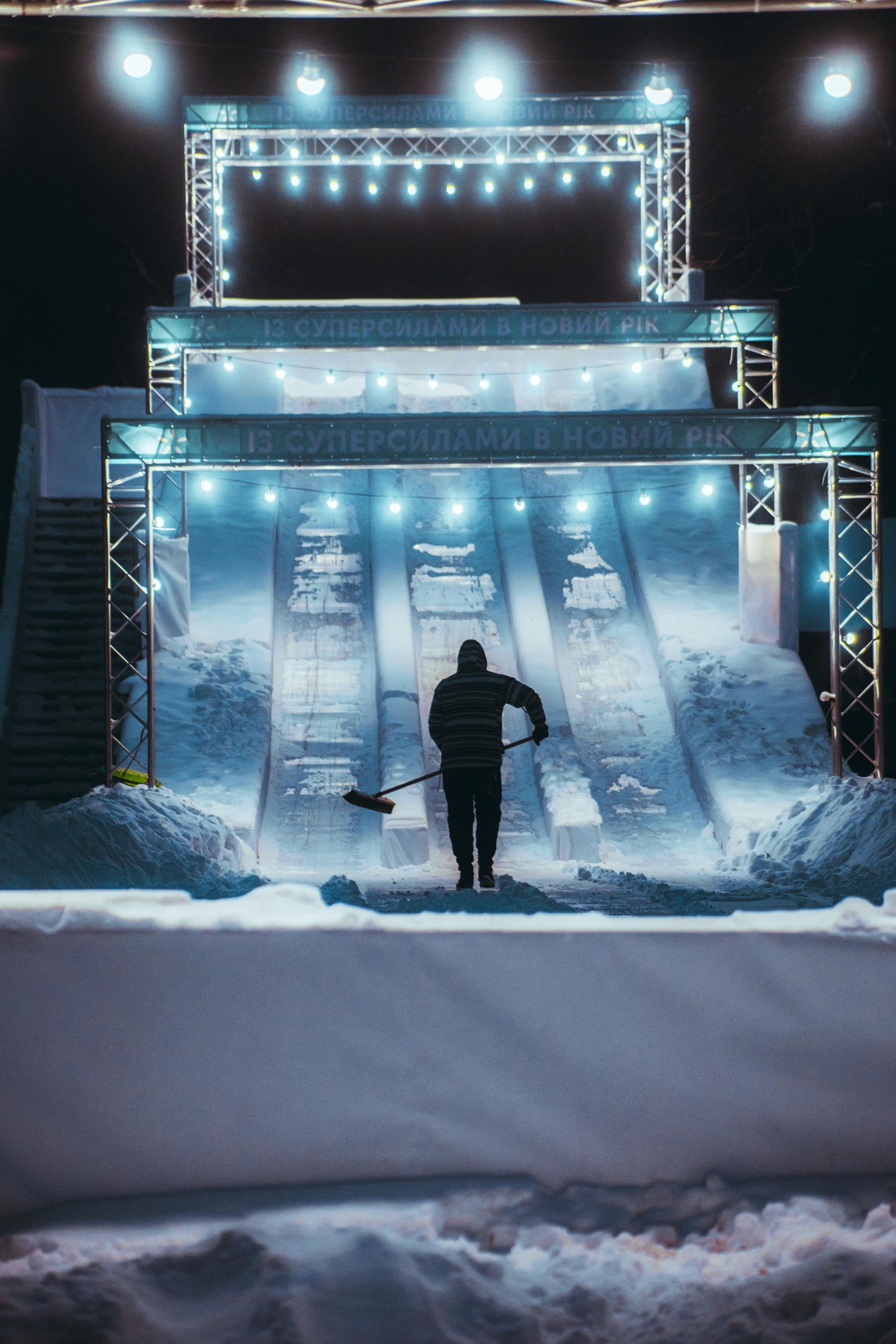 A man is shoveling snow in front of a snow slide at night.