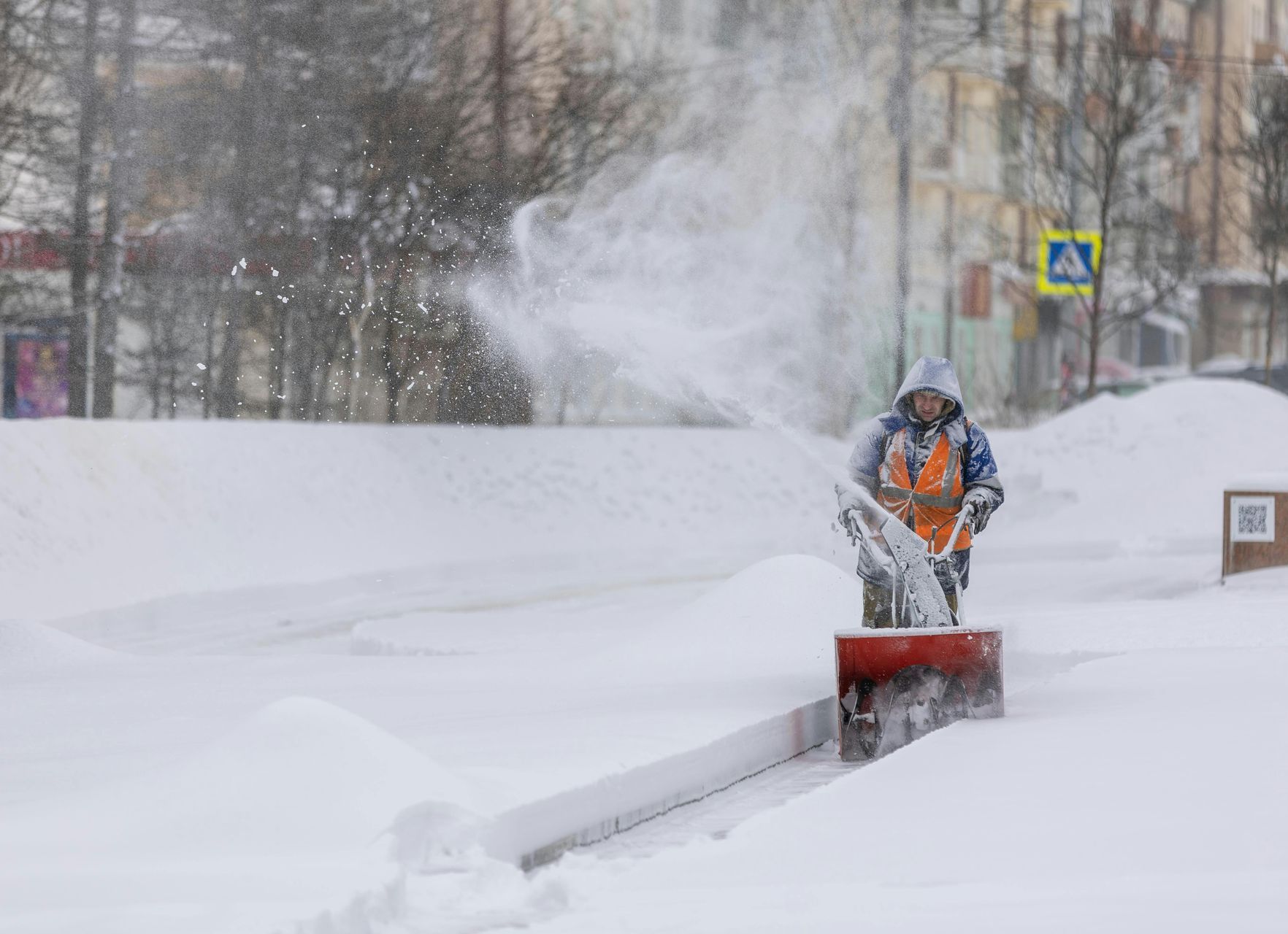 Man is using a snow blower to remove snow from sidewalk
