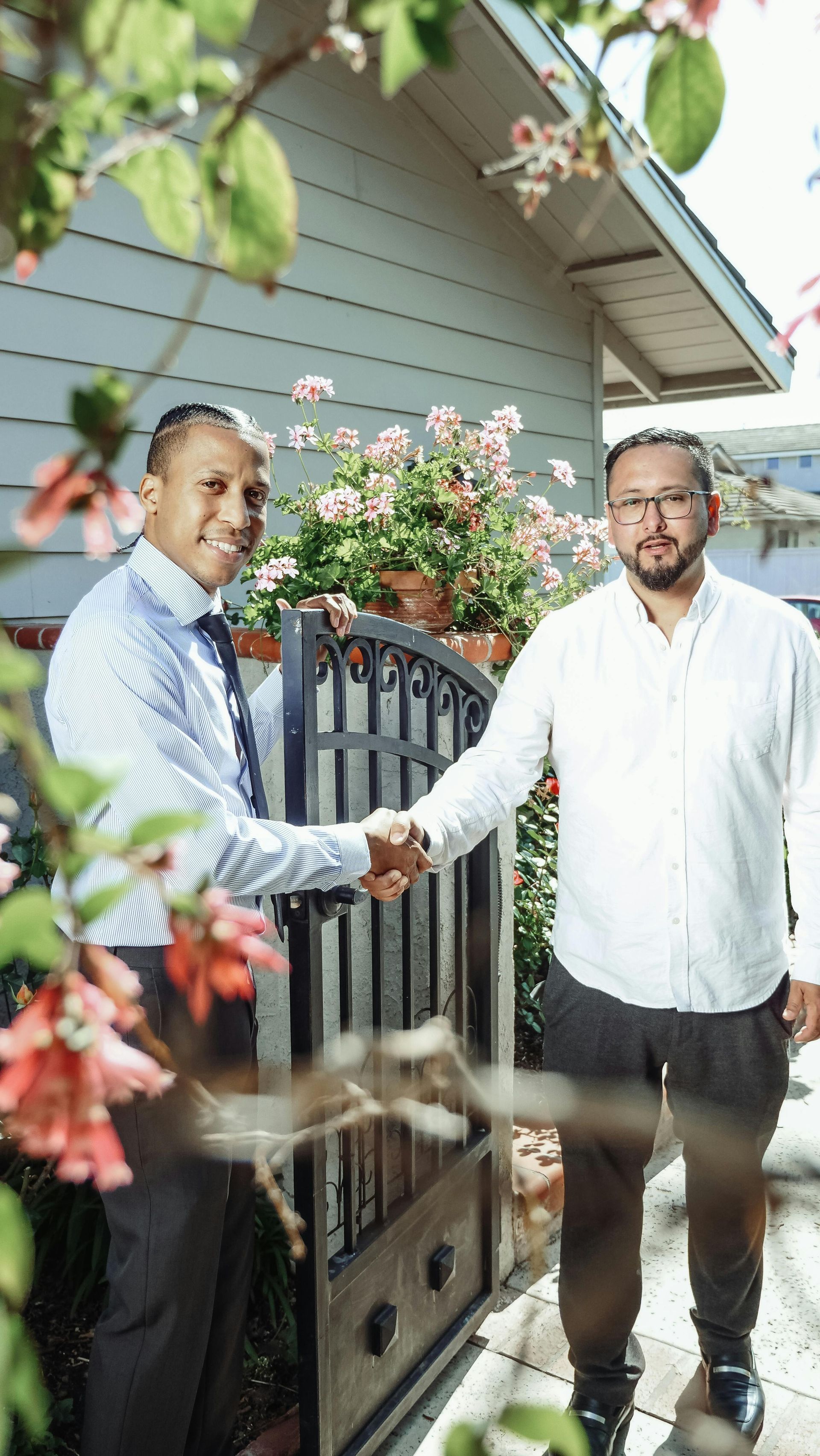 Two men are shaking hands in front of a house.