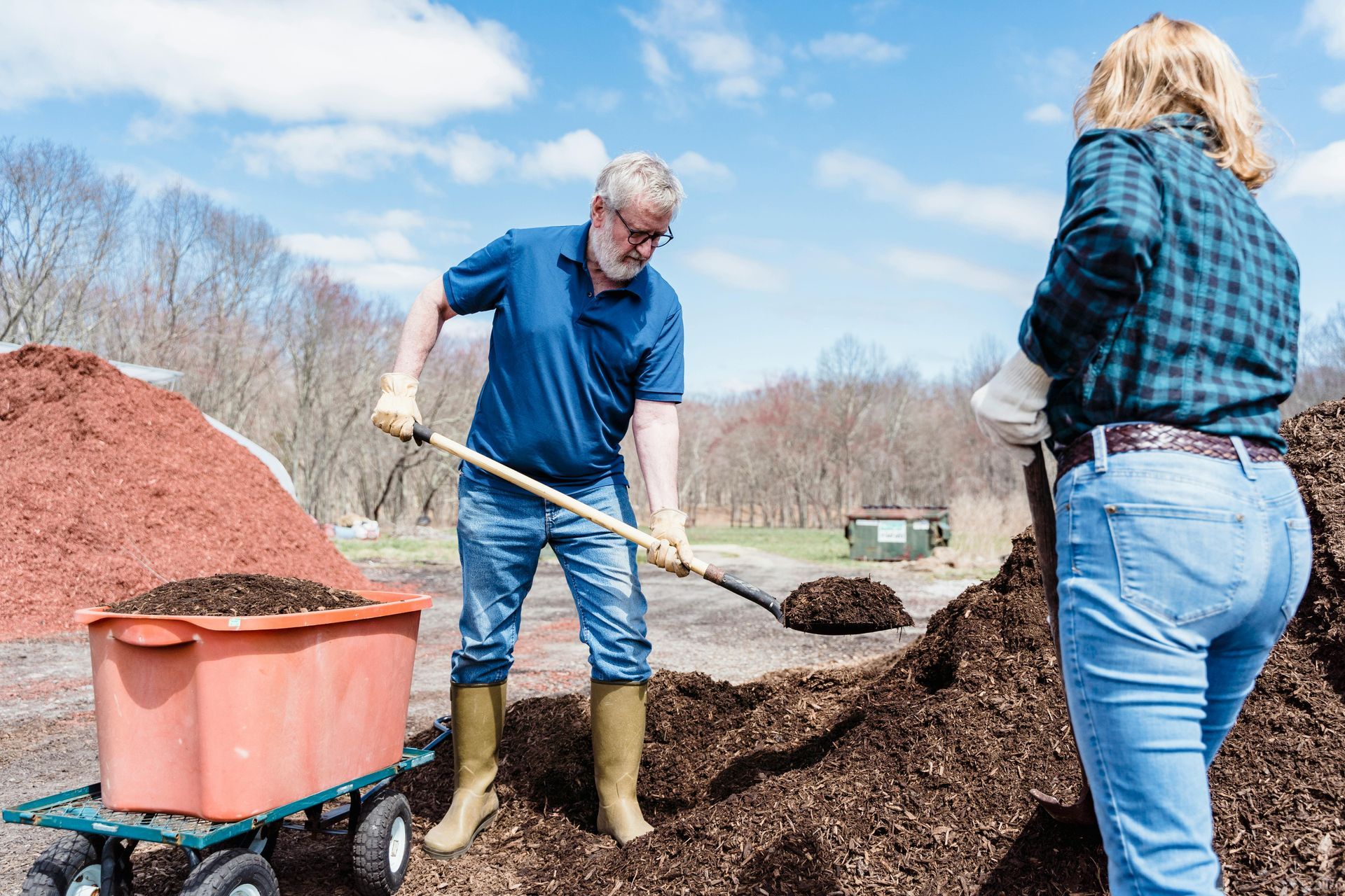 A man is shoveling dirt into a cart while a woman looks