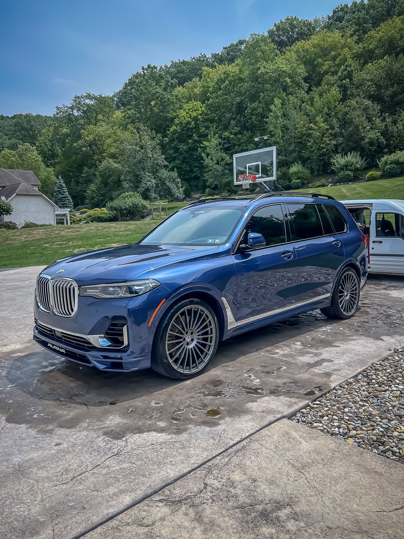 A blue bmw x7 is parked in a driveway next to a basketball hoop.
