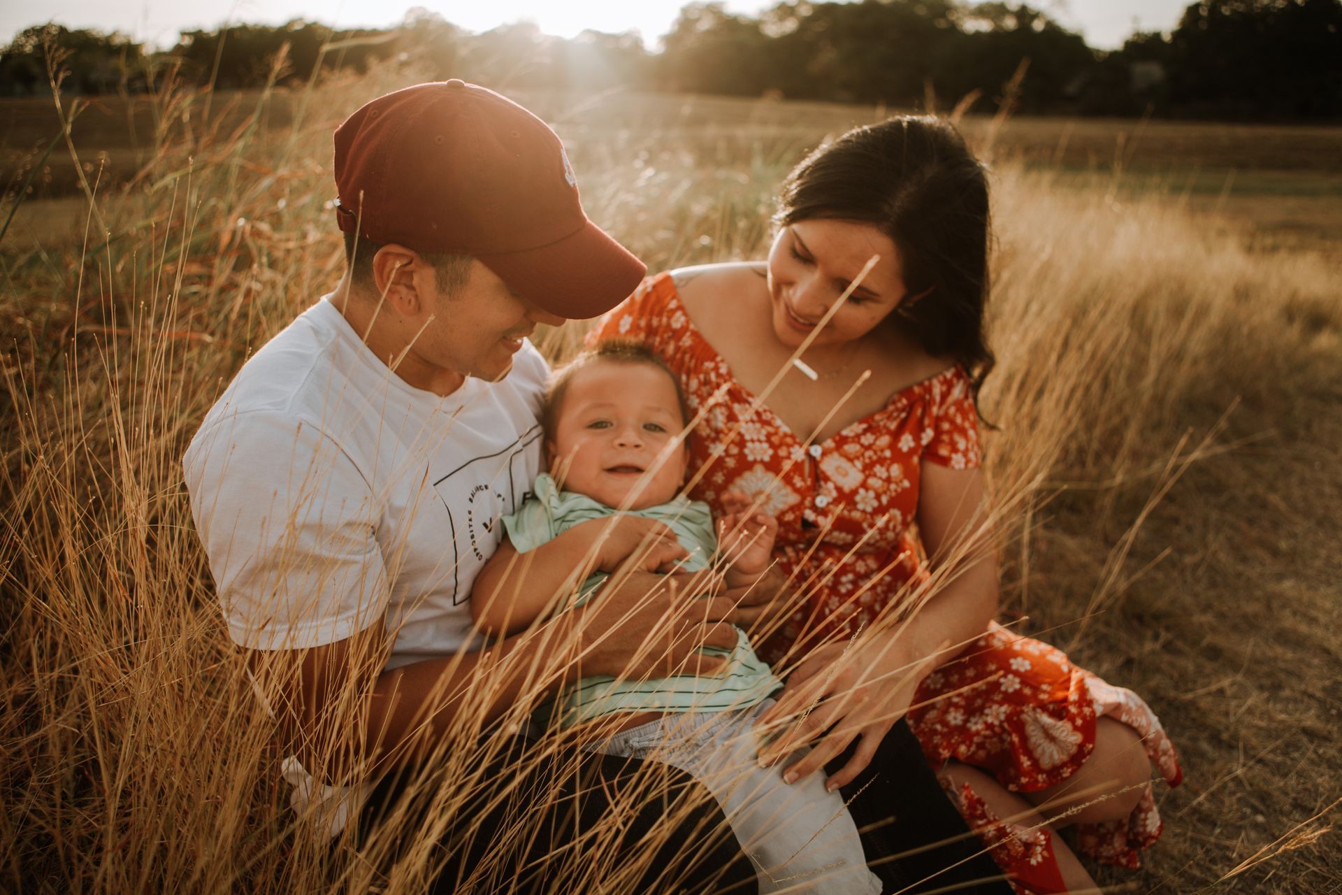 A family is sitting in a field holding a baby.