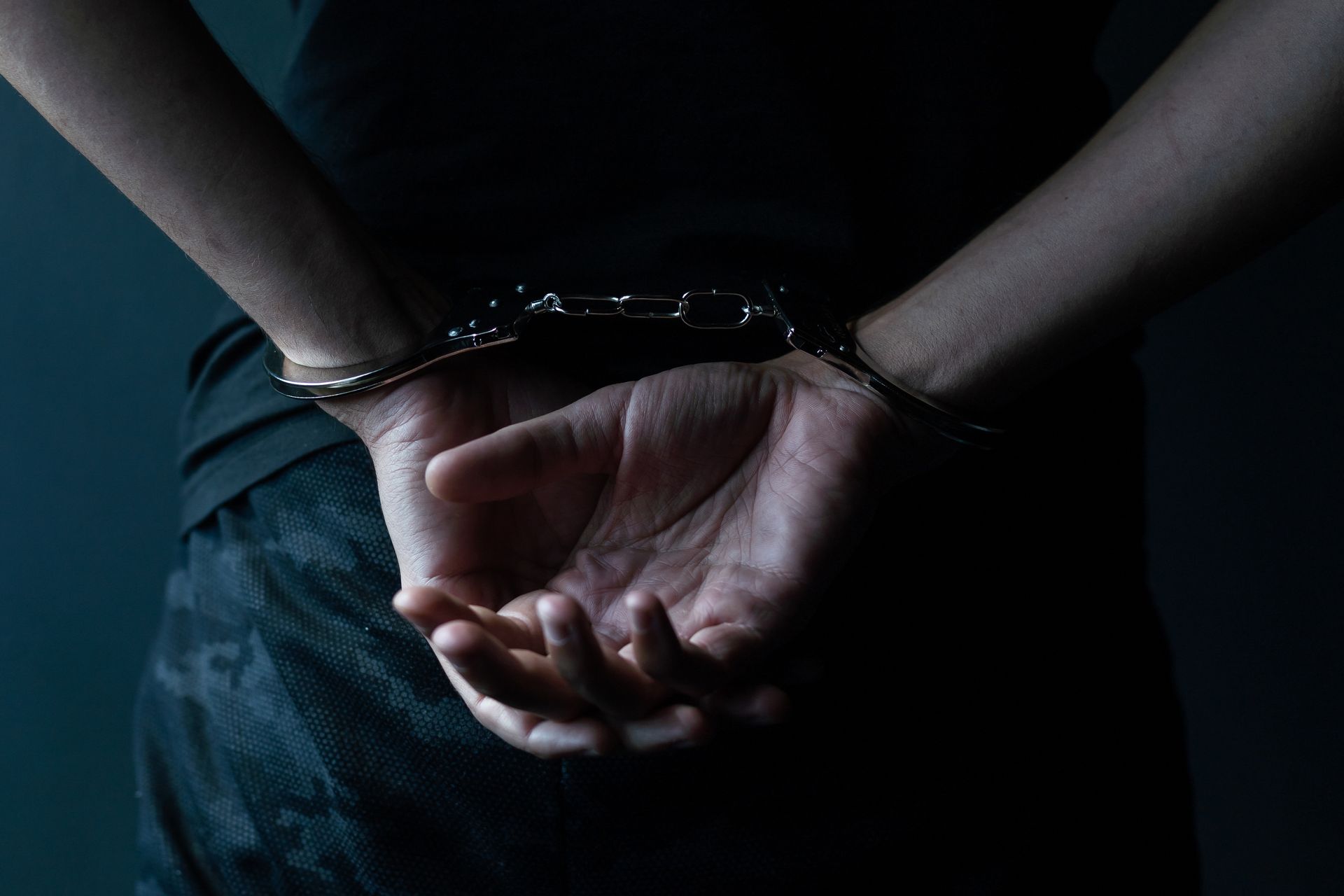 Person in handcuffs, hands behind their back, dark clothing.