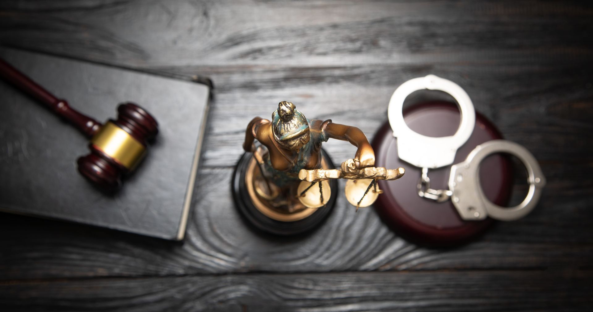 Gavel, brass scales, and handcuffs on a dark wooden desk