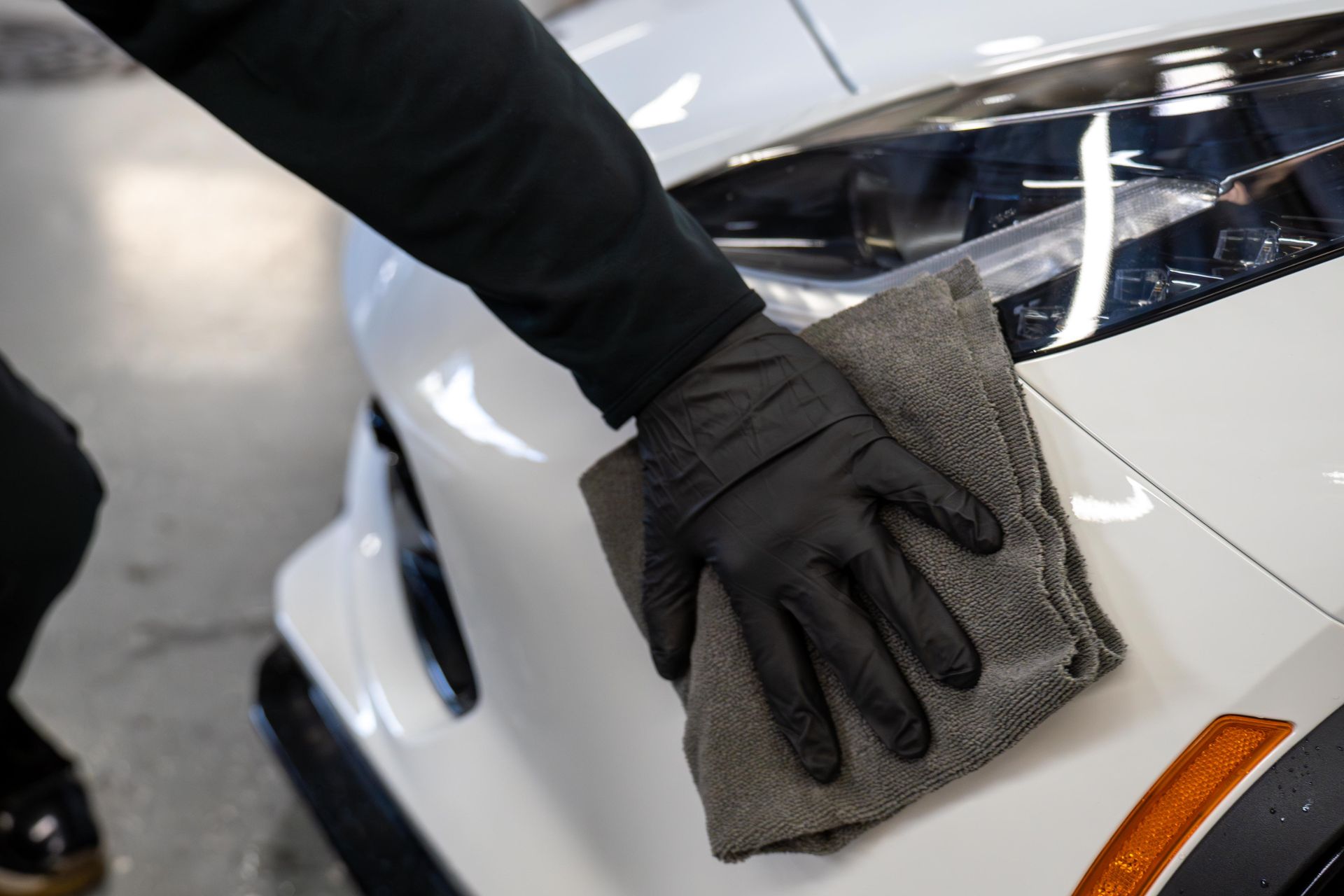 Person in black glove cleaning white car with gray cloth.