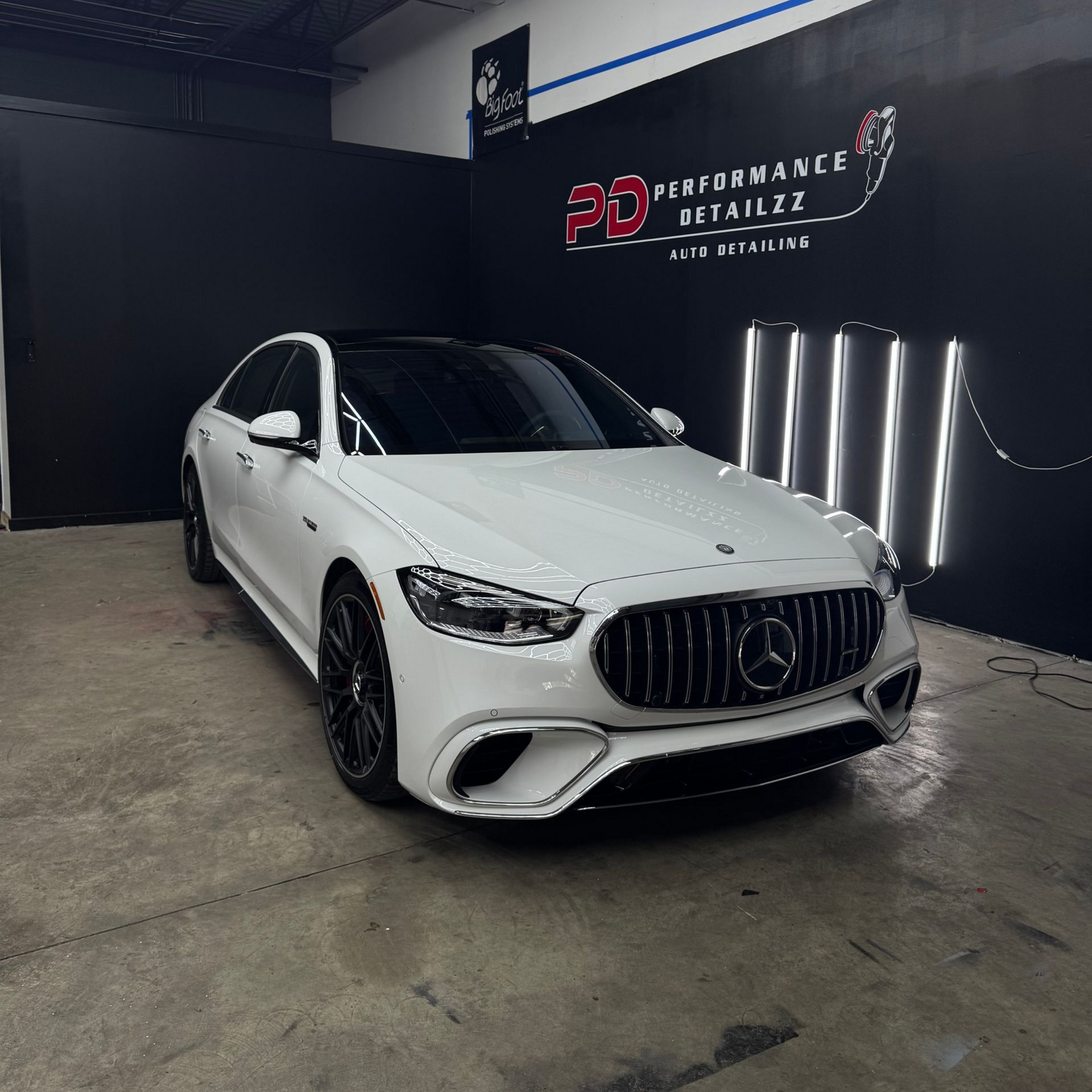 White Mercedes-Benz sedan in a car detailing shop, parked under bright lights.
